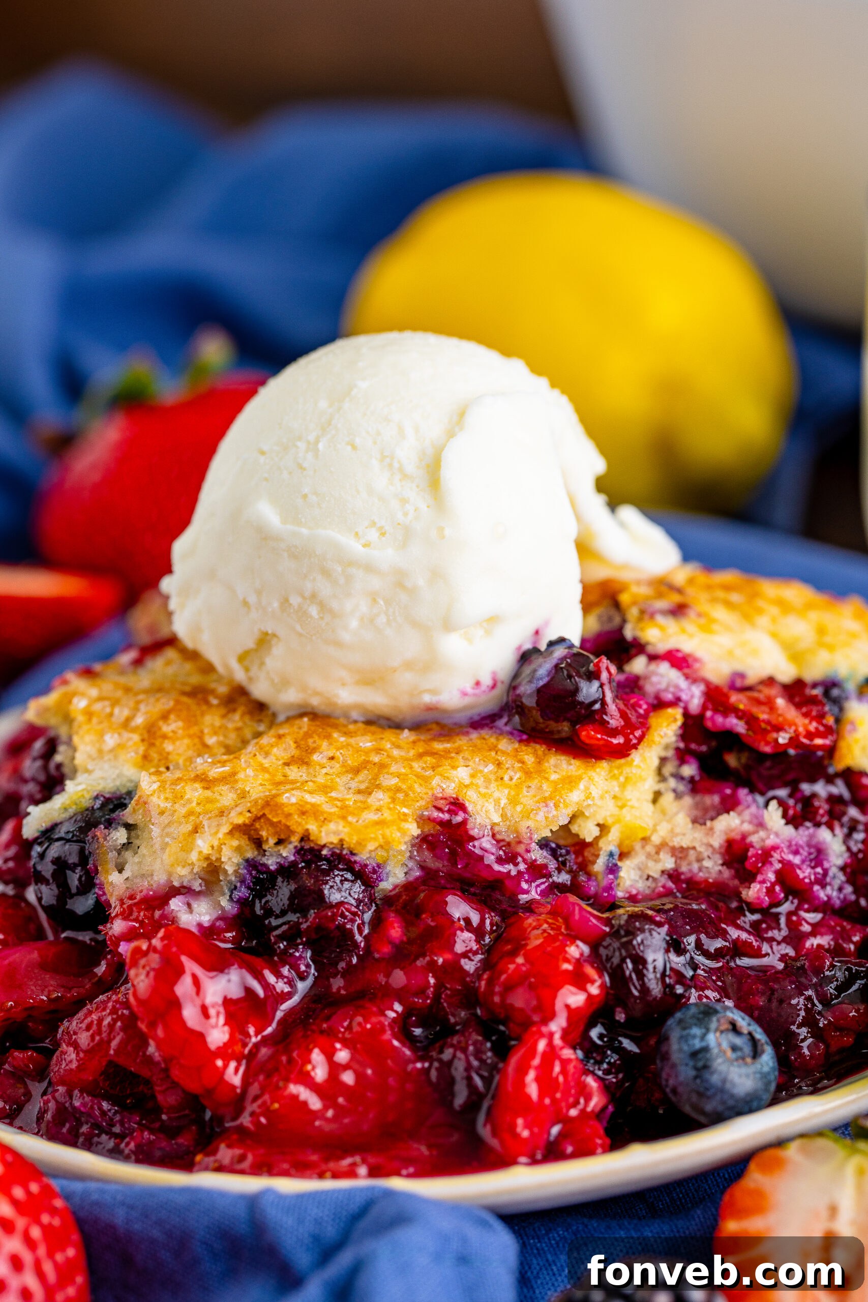 Close up view of the golden, crusty topping of a Mixed Berry Cobbler, revealing hints of the vibrant berry filling bubbling underneath.
