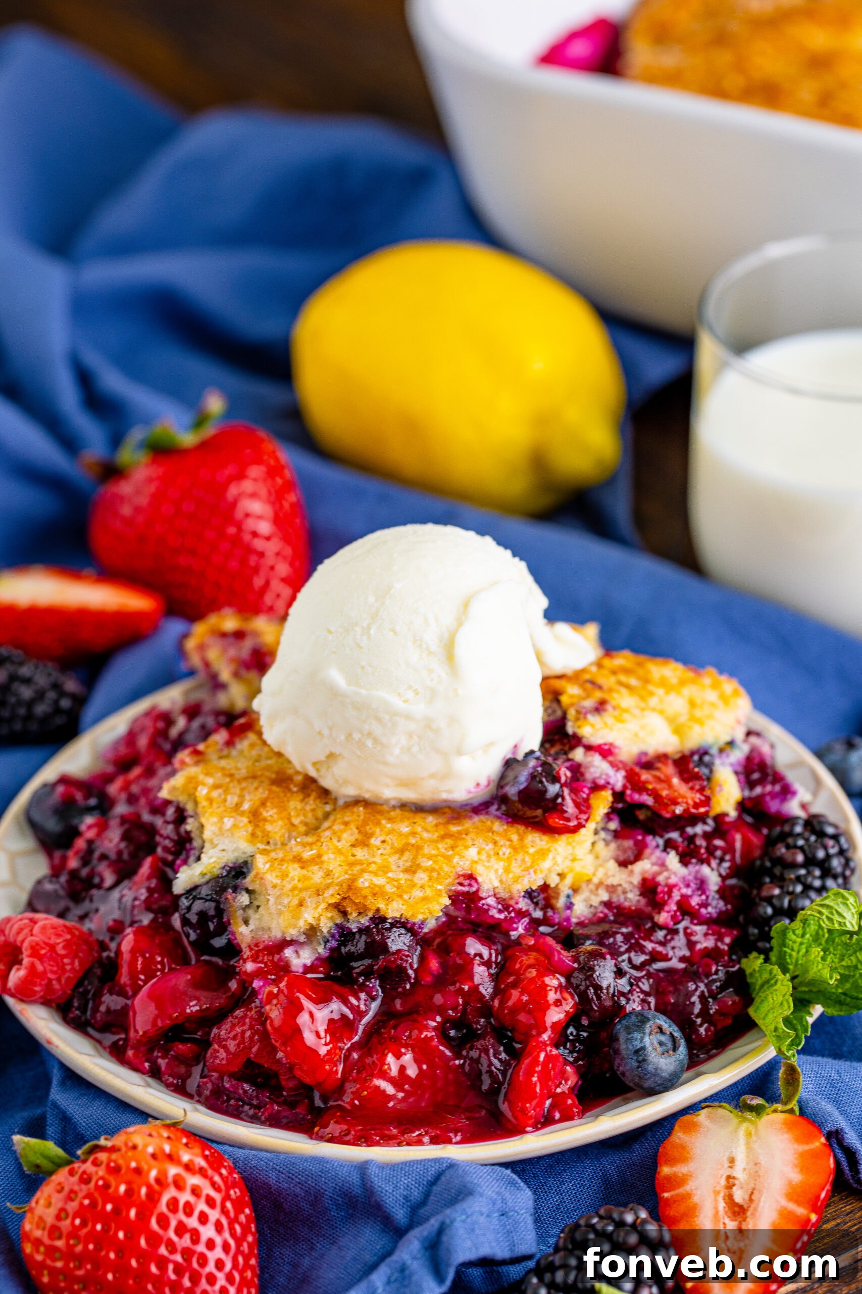 Front view of a Mixed Berry Cobbler in a white baking dish, presented beautifully with a scoop of vanilla ice cream, ready for a gathering.