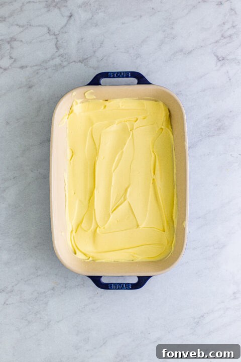 Smoothing out the final layer of fluffy whipped topping over the entire banana icebox cake, creating a pristine white surface before chilling.