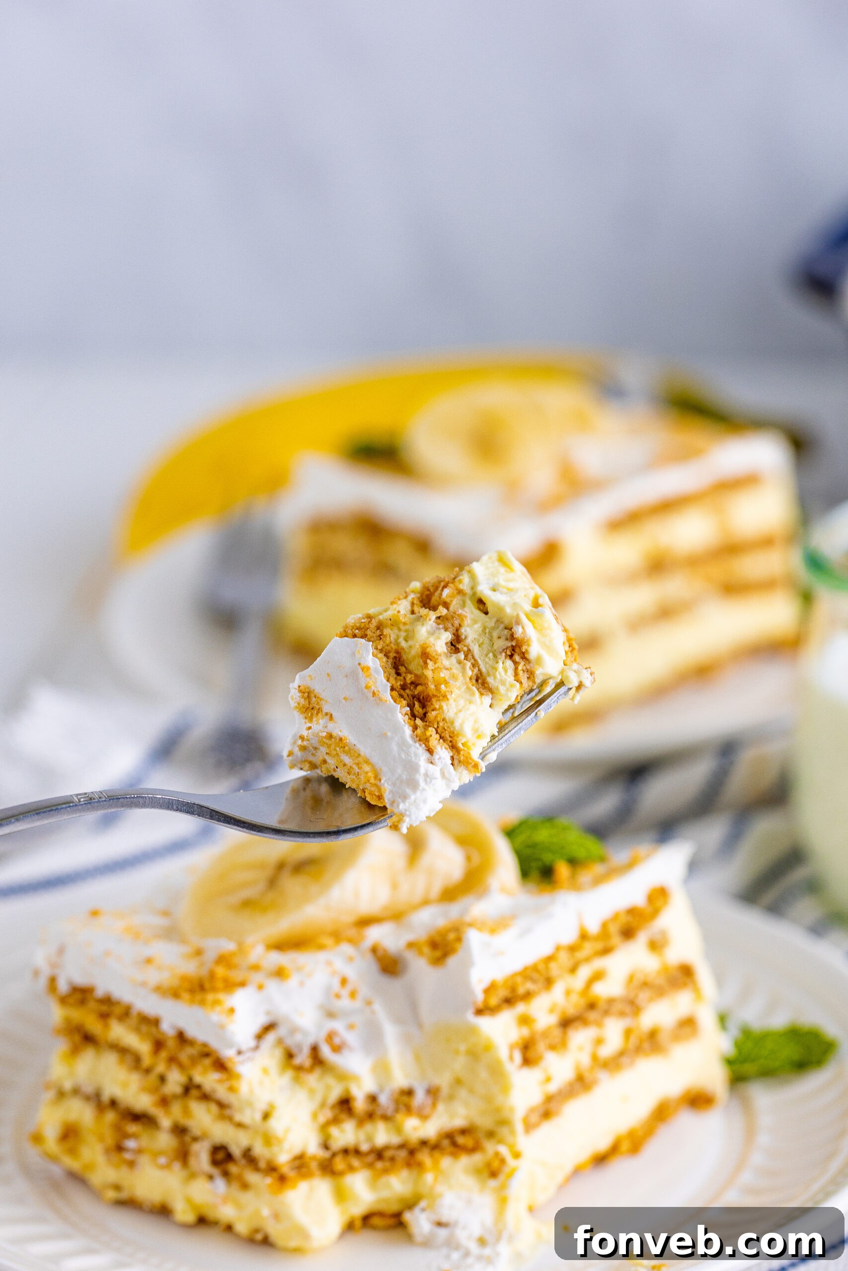 A close-up side view of a perfect bite of Banana Icebox Cake held on a silver fork, showcasing the distinct creamy and cookie layers.