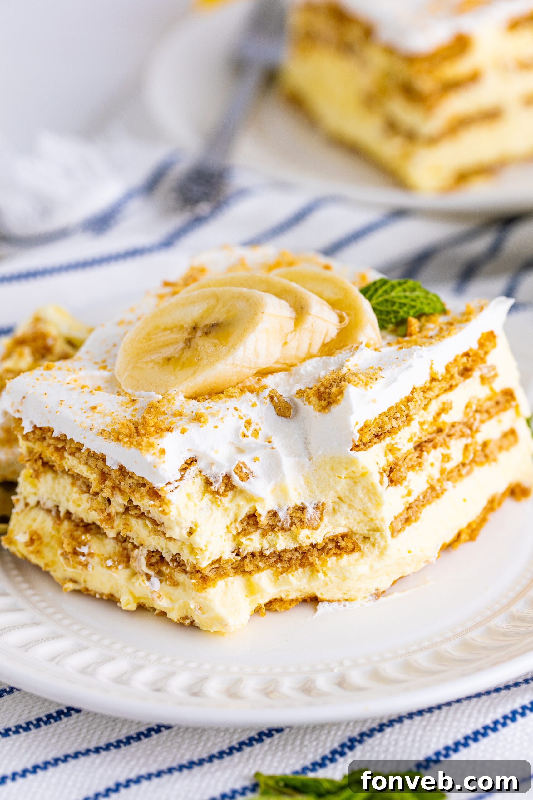 An inviting image of a slice of Banana Icebox Cake on a white plate, with a fork having just scooped a bite, tempting viewers to try a piece.