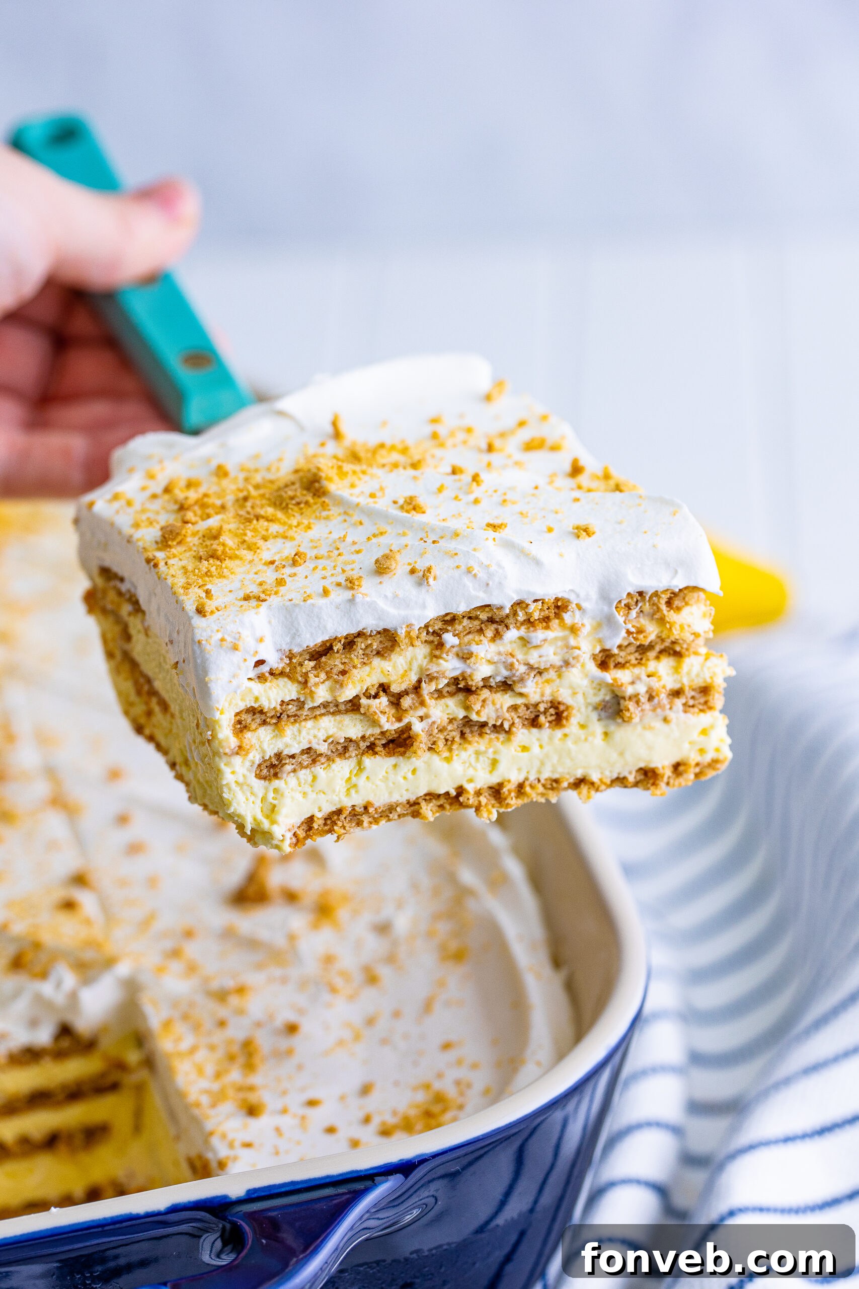 A close-up view of a generous slice of homemade Banana Icebox Cake being lifted from a serving dish with a spatula, showcasing its soft, layered texture.