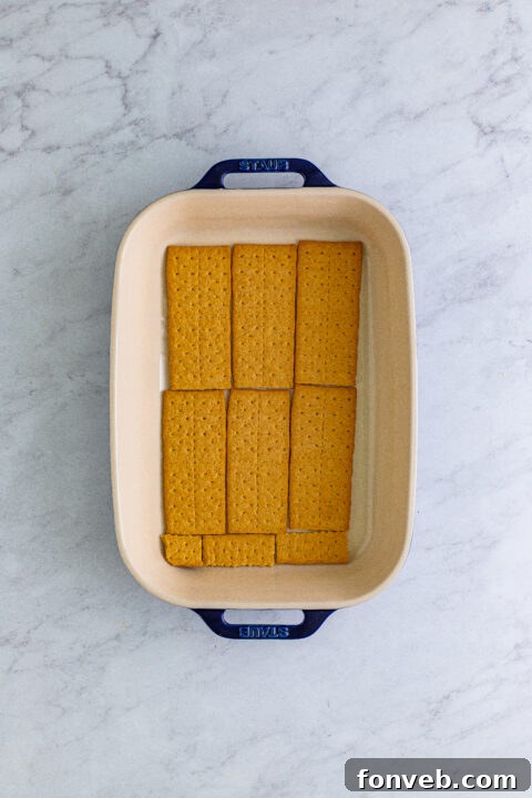 Carefully placing a second layer of graham crackers on top of the banana and pudding, forming the structural foundation of the icebox cake.