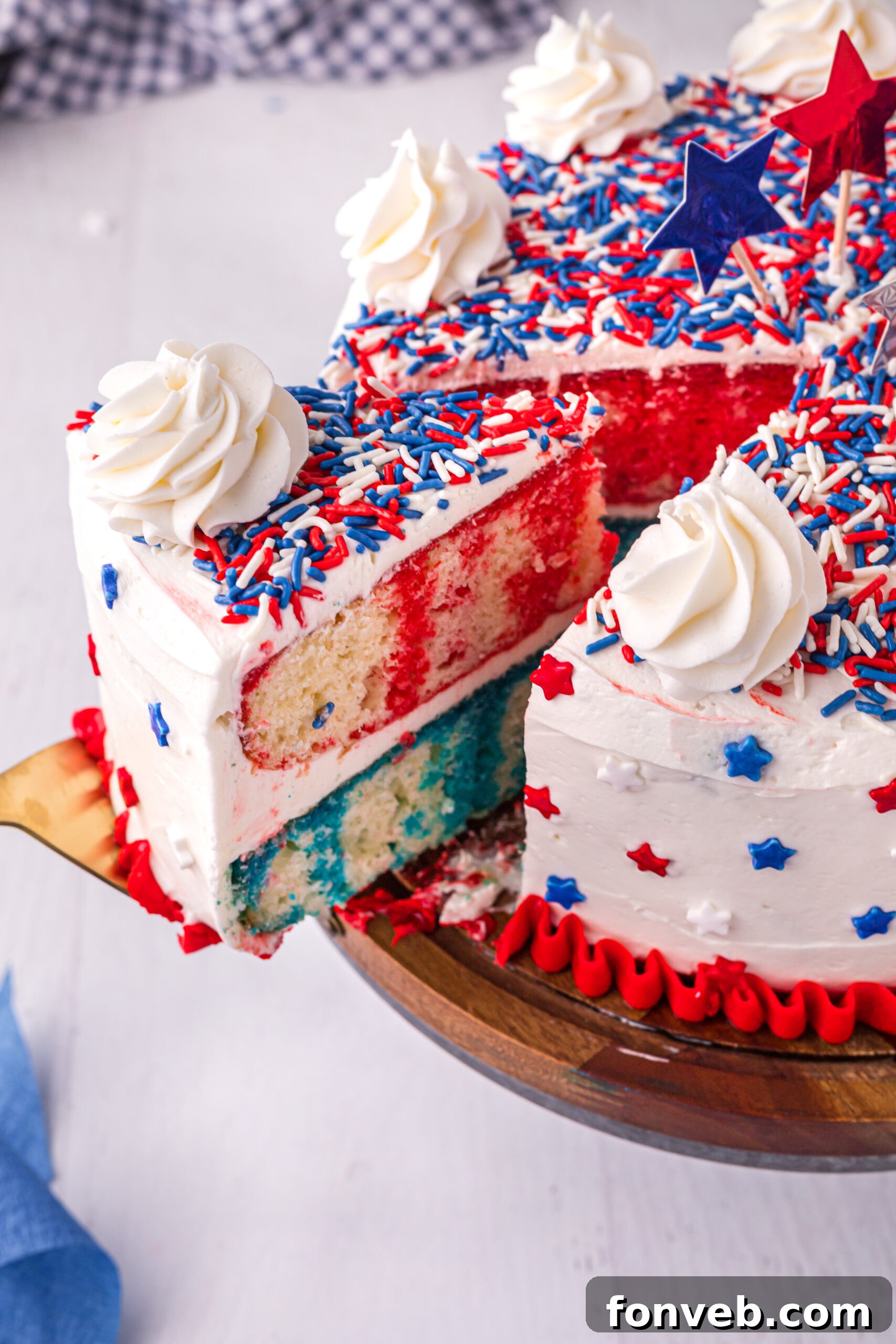 Side view of a slice being removed from the 4th of July Cake on a wooden stand, showing the vibrant layers.