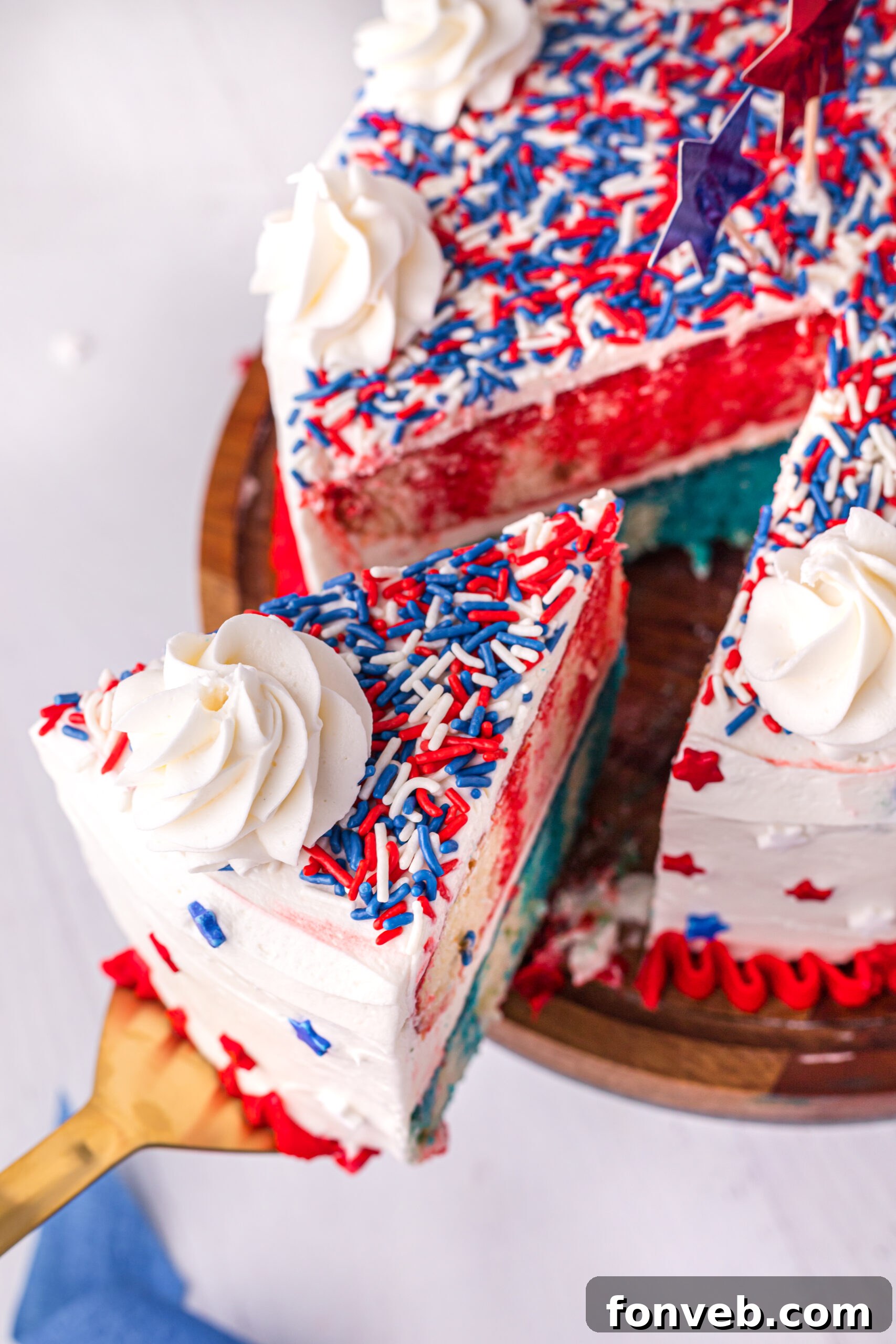 Close up view of a slice being served from the 4th of July Cake on a wooden stand, highlighting the red and blue Jell-O.
