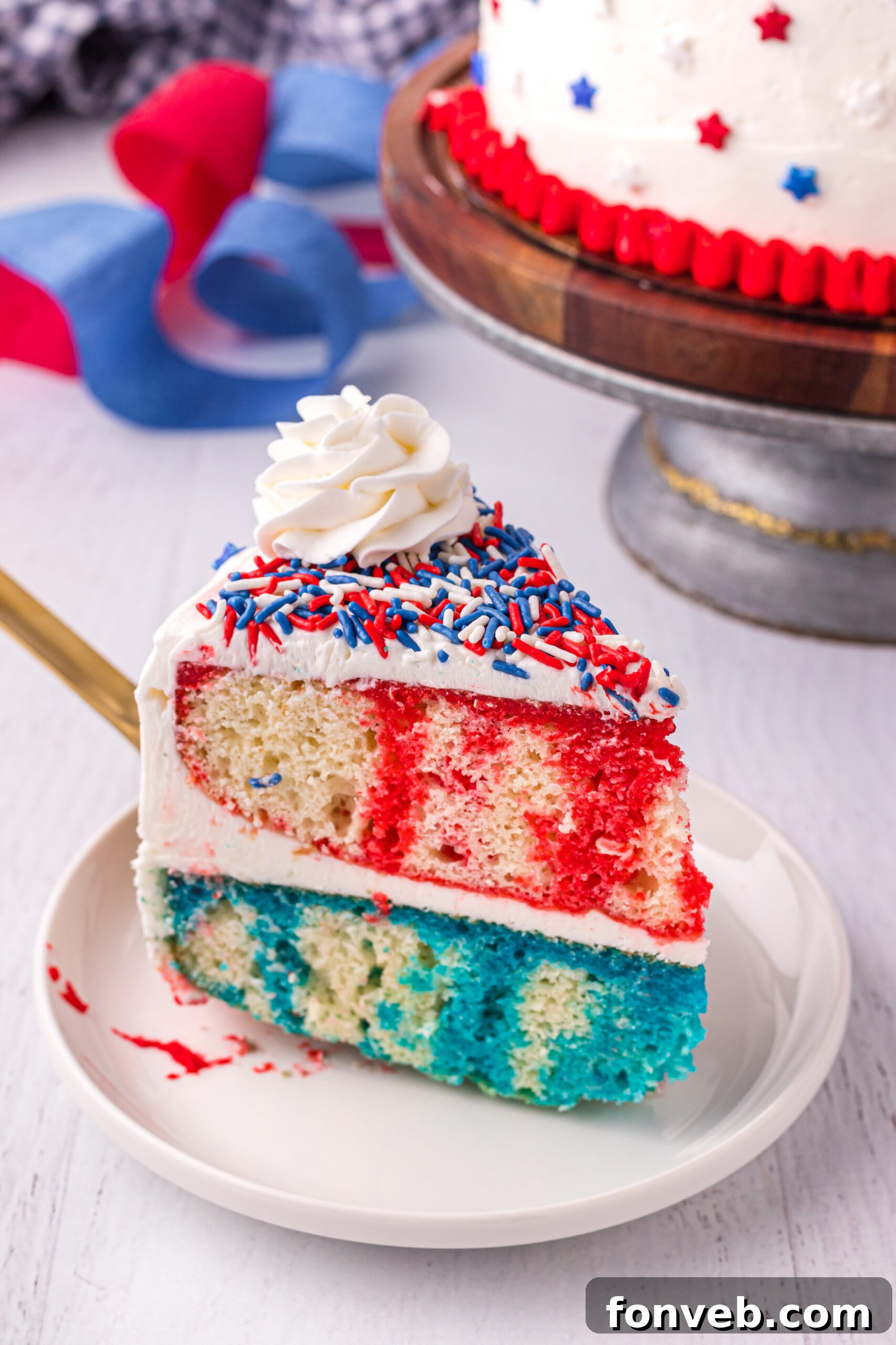 Front view of a perfectly sliced 4th of July Cake on a white plate, revealing the red and blue layers.