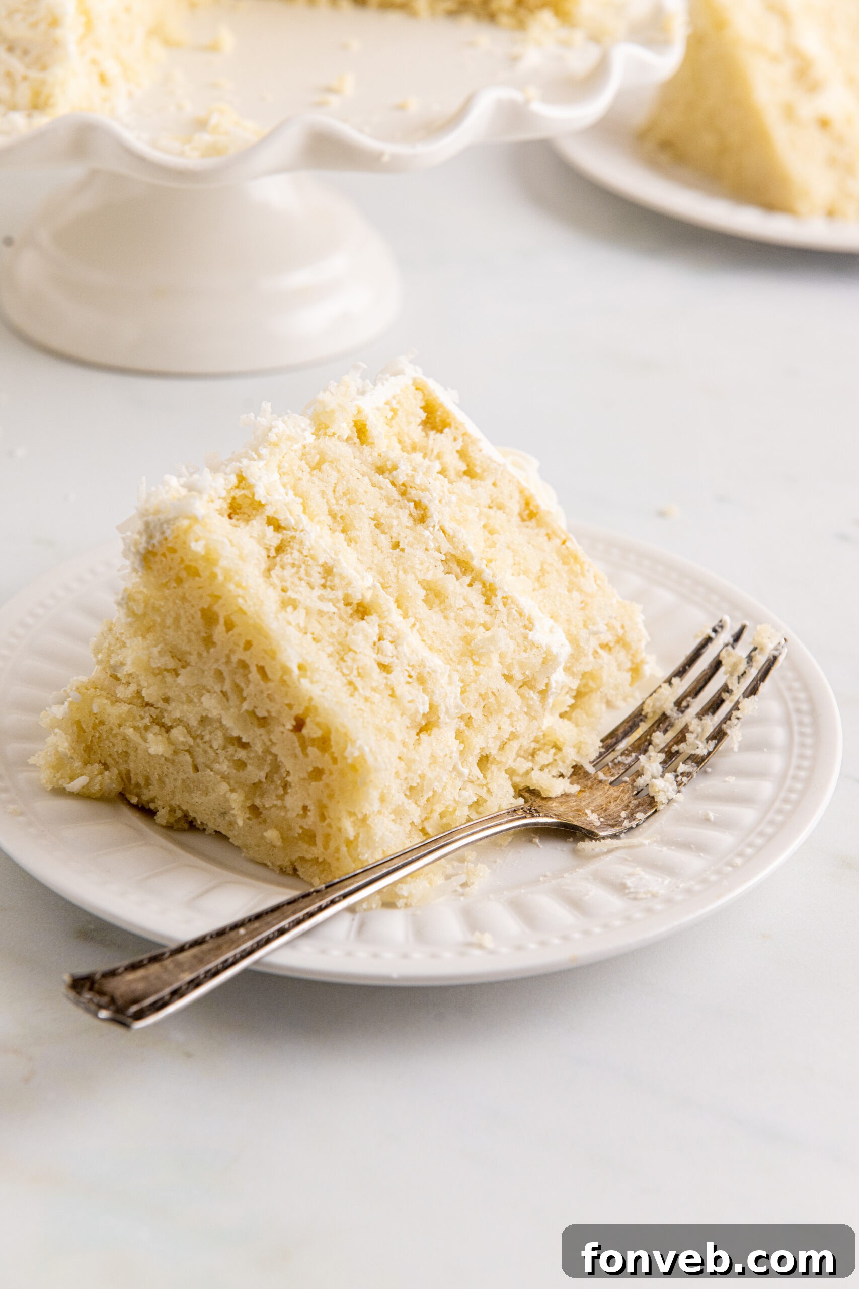 Tropical Coconut Dream Cake 16 Overhead view of a delectable slice of Coconut Layer Cake on a white plate, with a bite removed, revealing the soft texture.