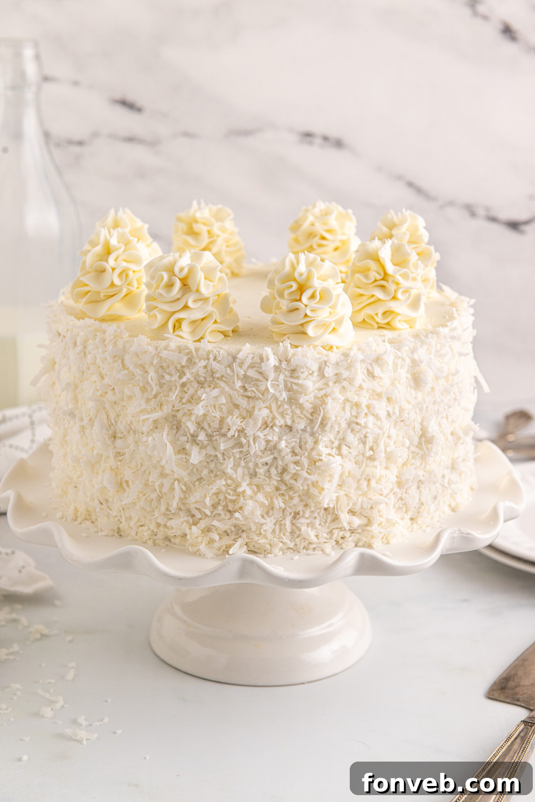 Tropical Coconut Dream Cake 3 Front view of a perfectly frosted Coconut Layer Cake on a pristine white cake stand, ready to be served.