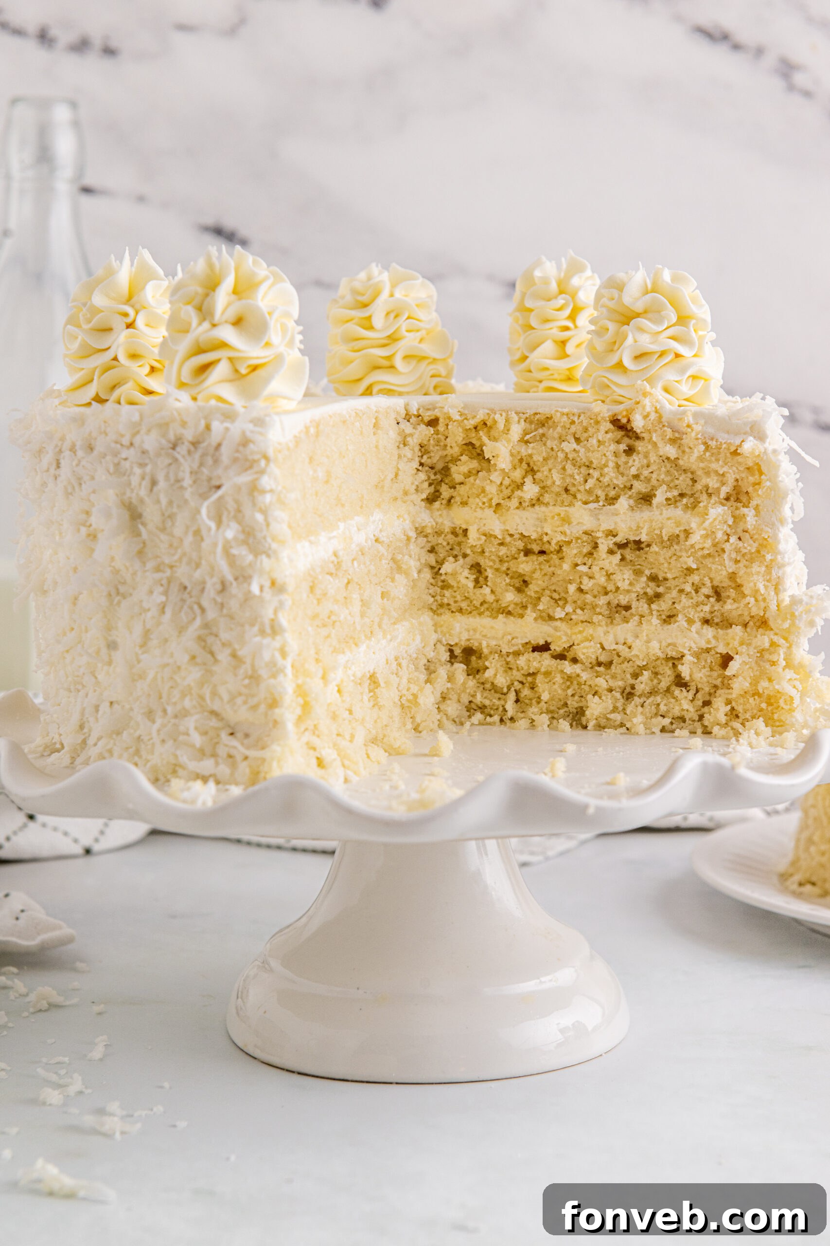 Tropical Coconut Dream Cake 6 Front view of a Coconut Layer Cake on a white cake stand with two inviting slices already removed, highlighting its rich layers.