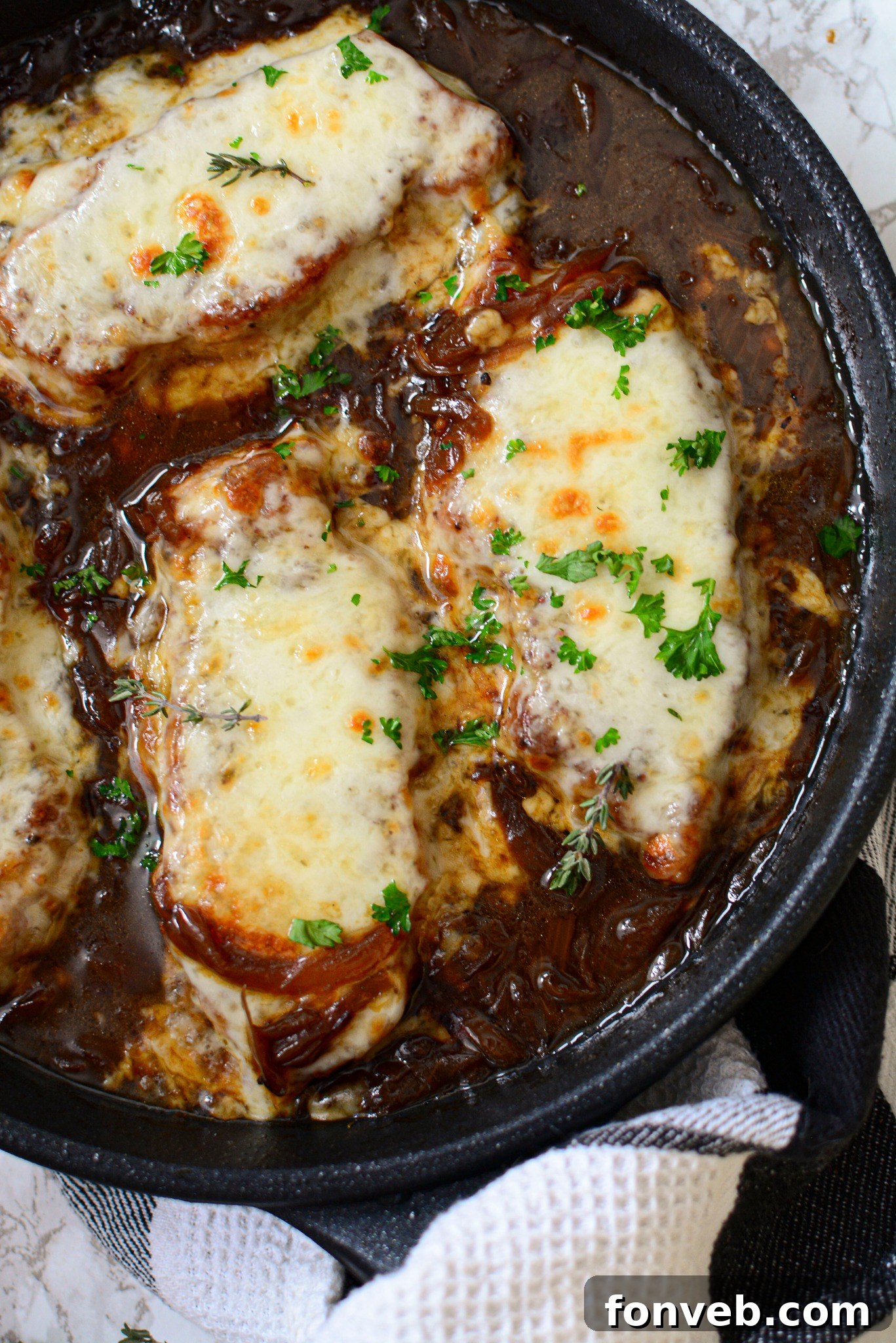 Close up view of perfectly seared French Onion Pork Chops, bathed in a rich, golden-brown caramelized onion gravy, nestled in a rustic cast iron skillet.