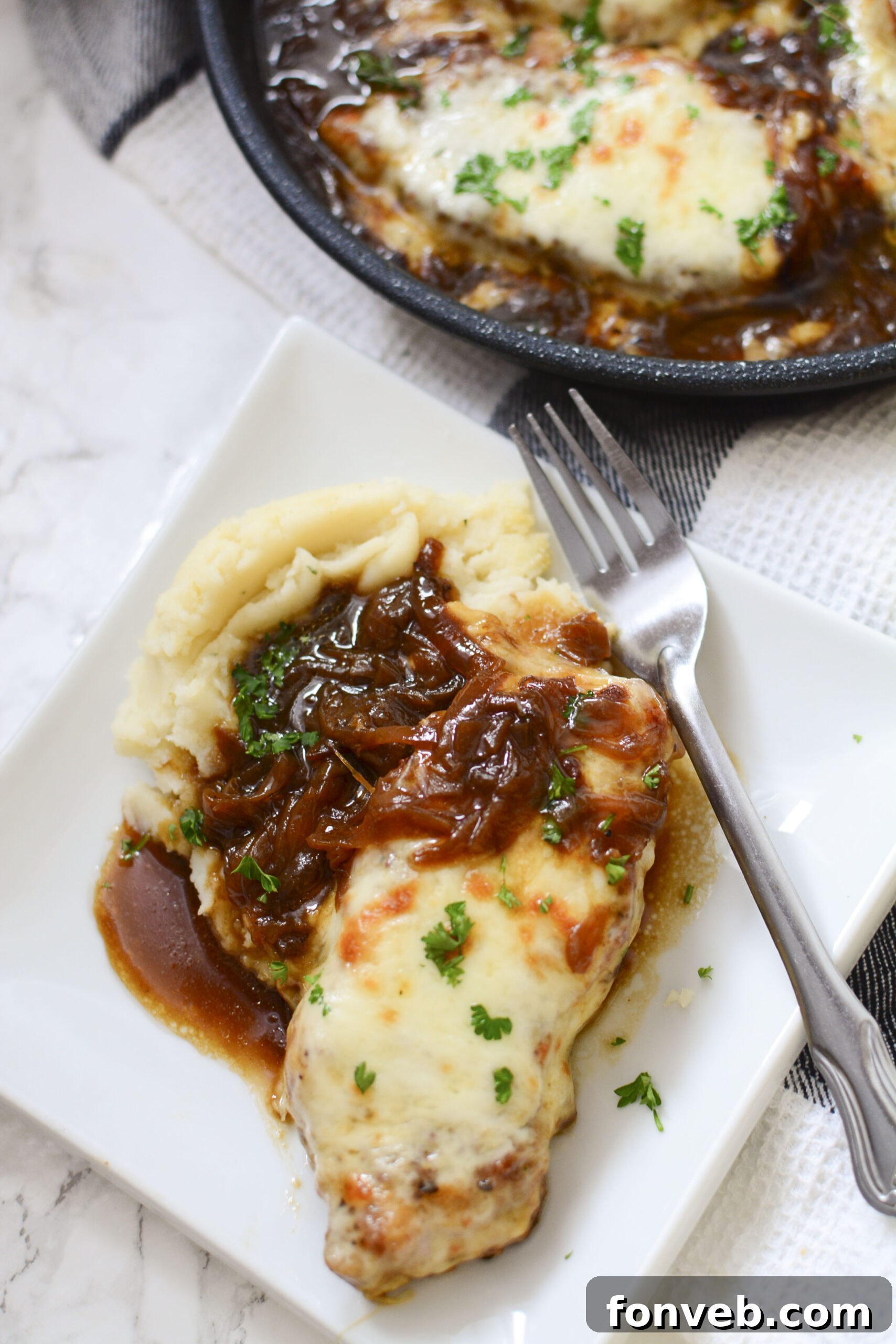 Overhead view of French Onion Pork Chops served with creamy mashed potatoes on a white plate, with a silver fork.