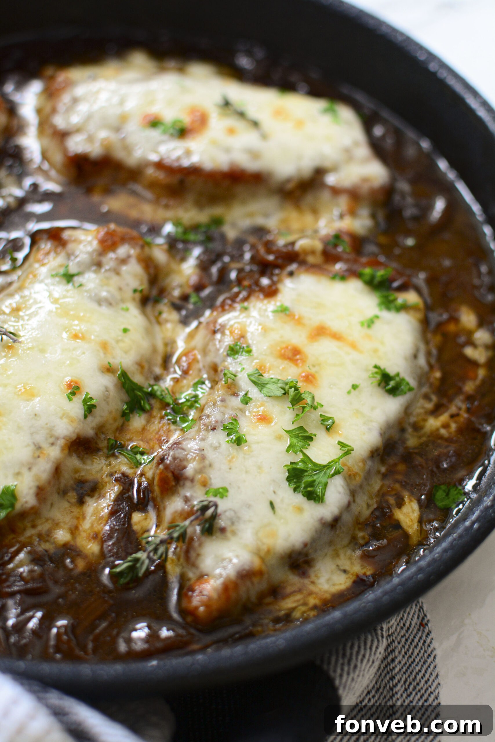 A different close-up perspective of French Onion Pork Chops in a cast iron skillet, highlighting the glistening sauce and tender meat.