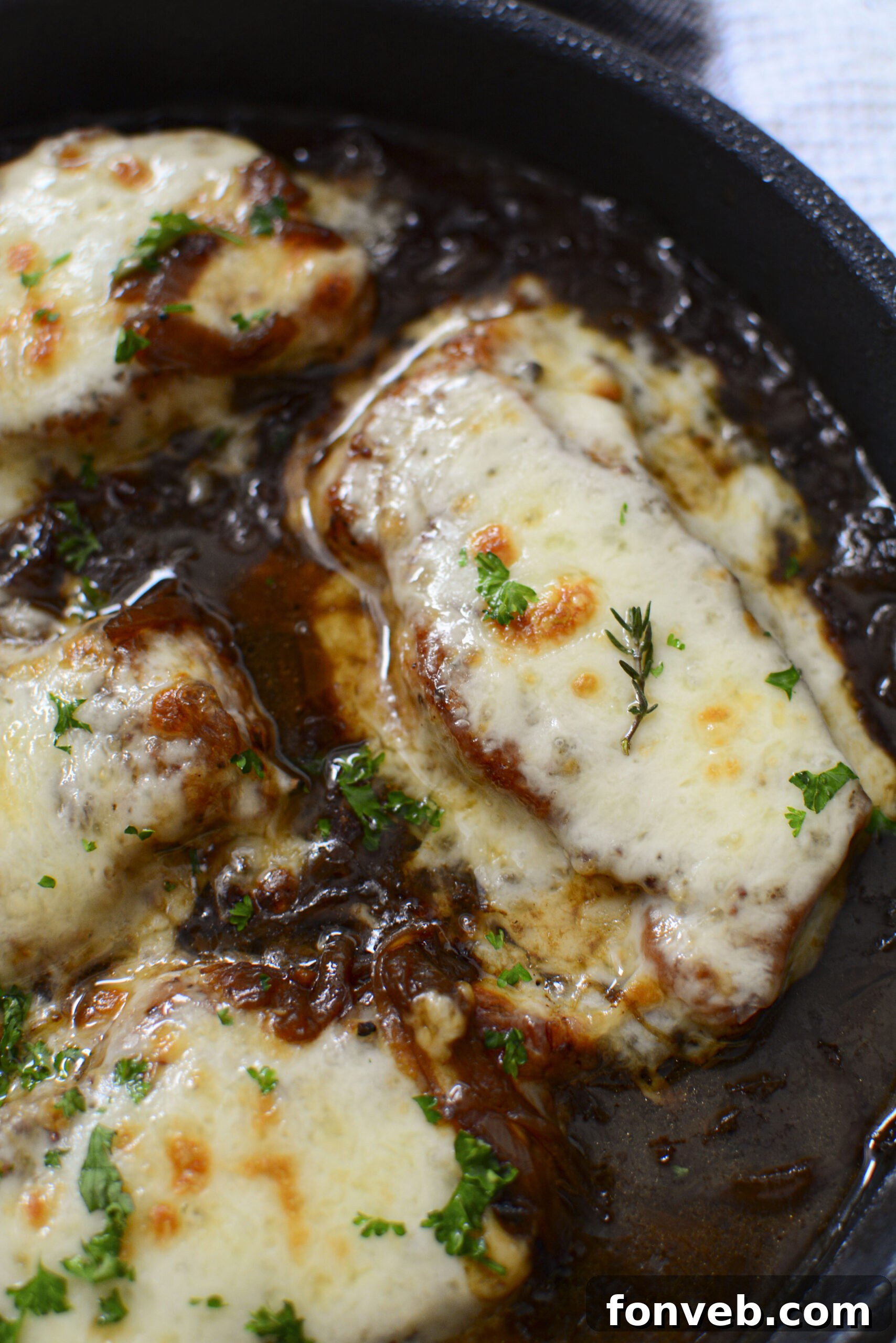 Overhead shot of French Onion Pork Chops with melted provolone cheese, just out of the oven in a cast iron skillet.