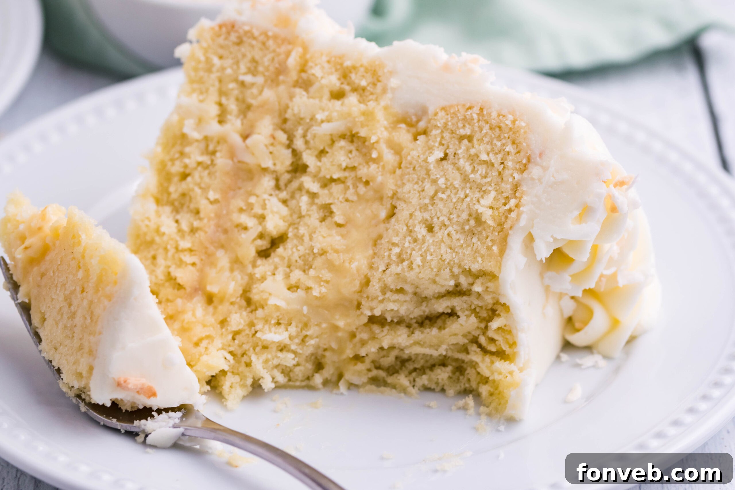 Front view of a slice of Coconut Custard Cake on a white plate with a bite removed by a silver fork.