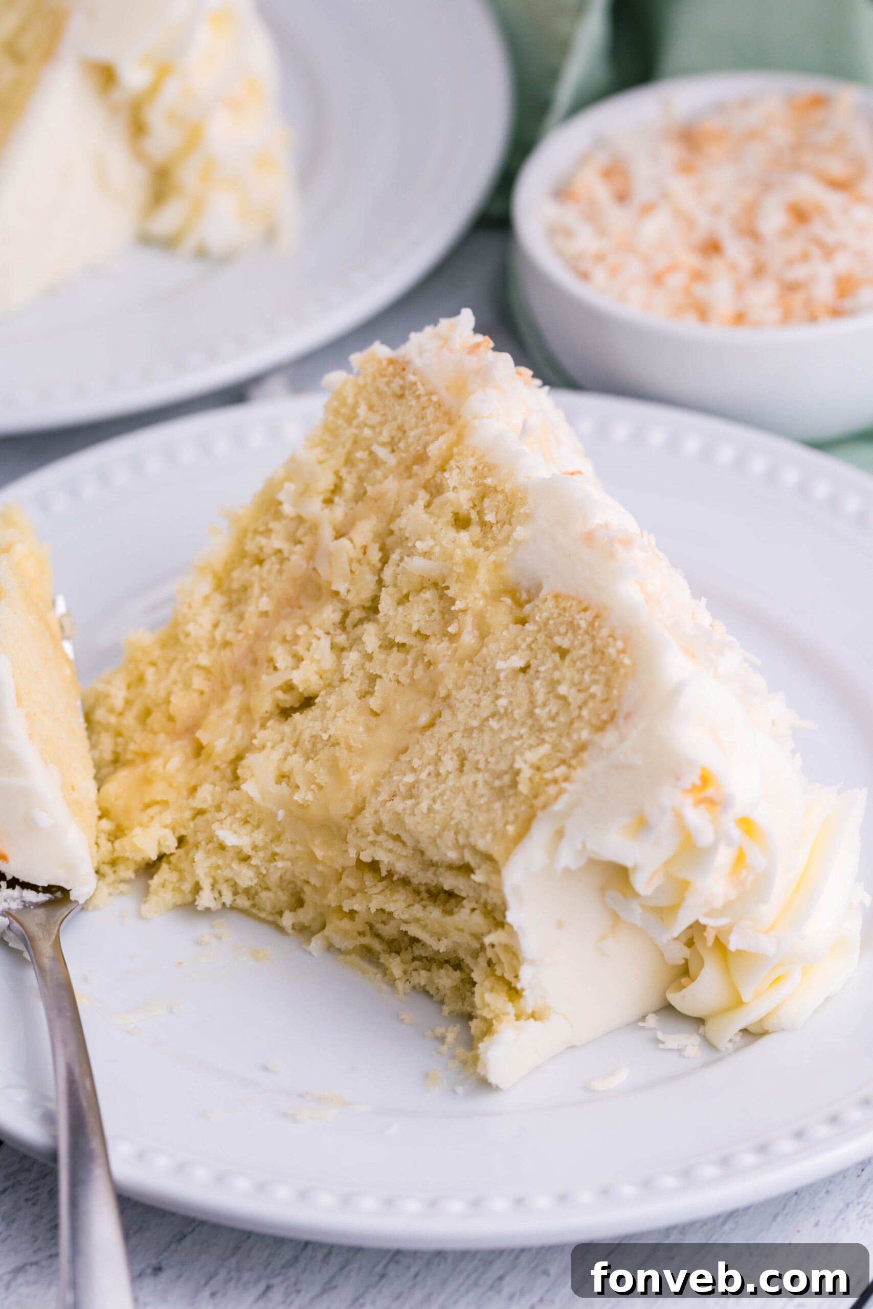 Front view of a slice of Coconut Custard Cake on a white plate with a bite removed by a silver fork.