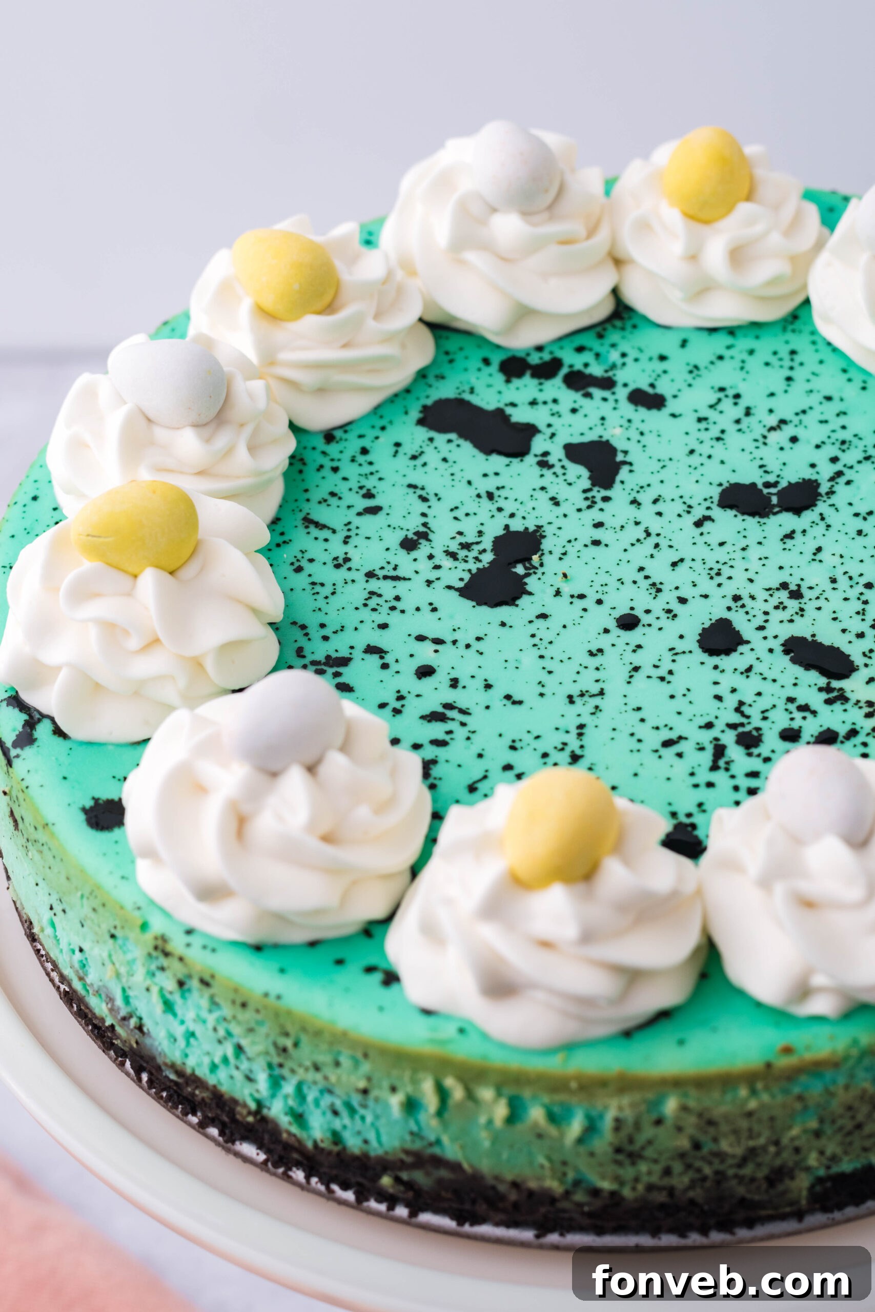 Close up view of Speckled Egg Cheesecake on a white cake stand, showcasing the beautiful teal and black speckles.