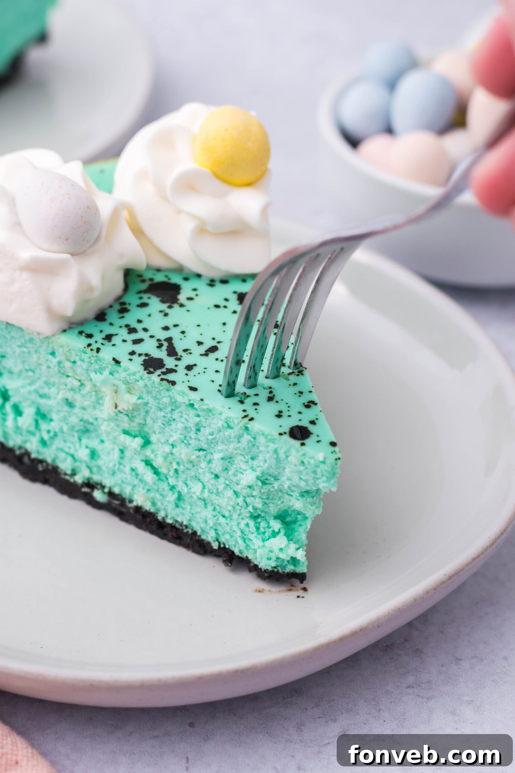 Close up view of a bite being removed from a slice of Speckled Egg Easter Cheesecake with a silver fork, highlighting its creamy interior.