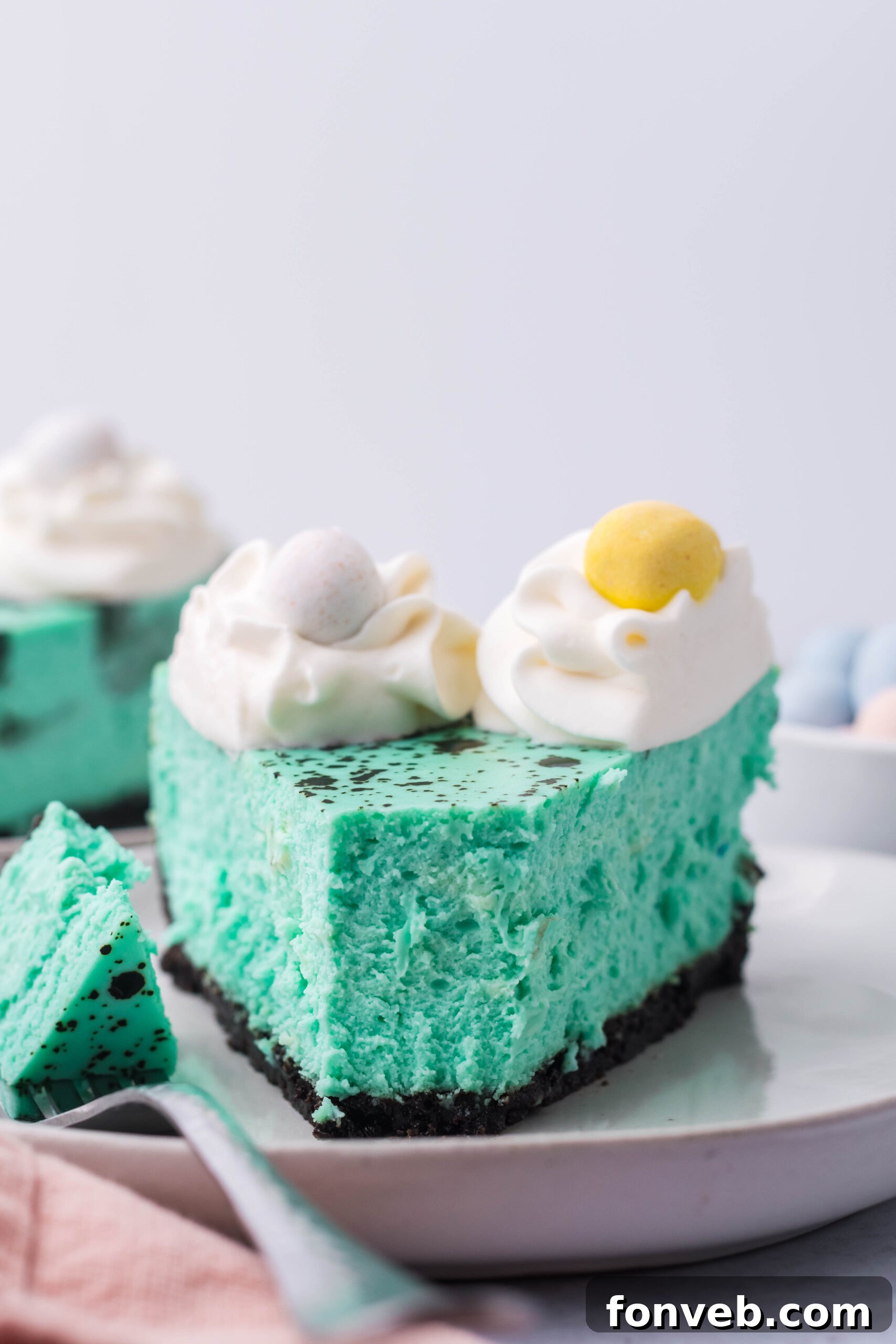 Front view of a slice of Speckled Egg Easter Cheesecake with a bite removed by a silver fork, ready to be enjoyed.