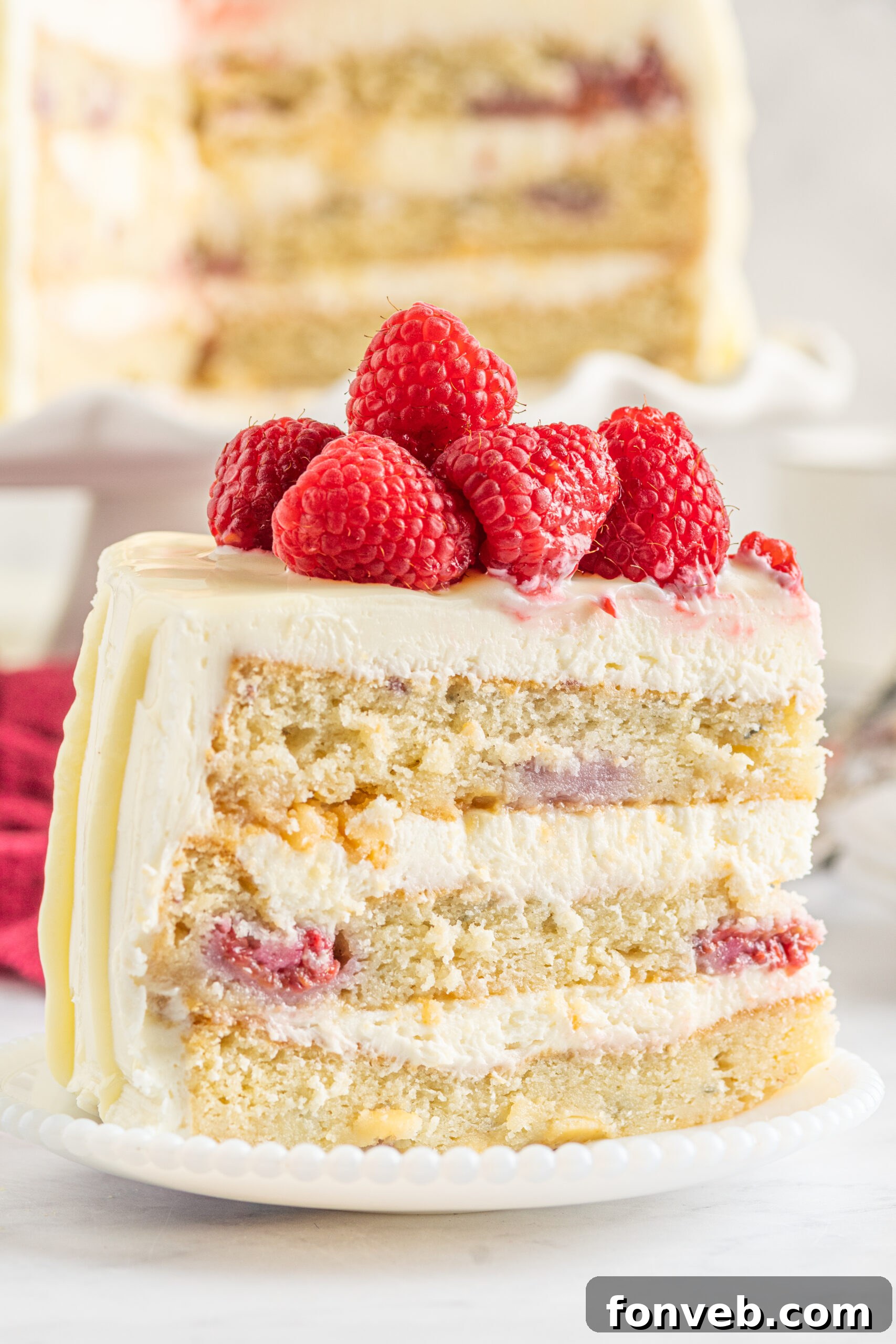 Side view of a slice of White Chocolate Cake with Raspberries on a white plate.