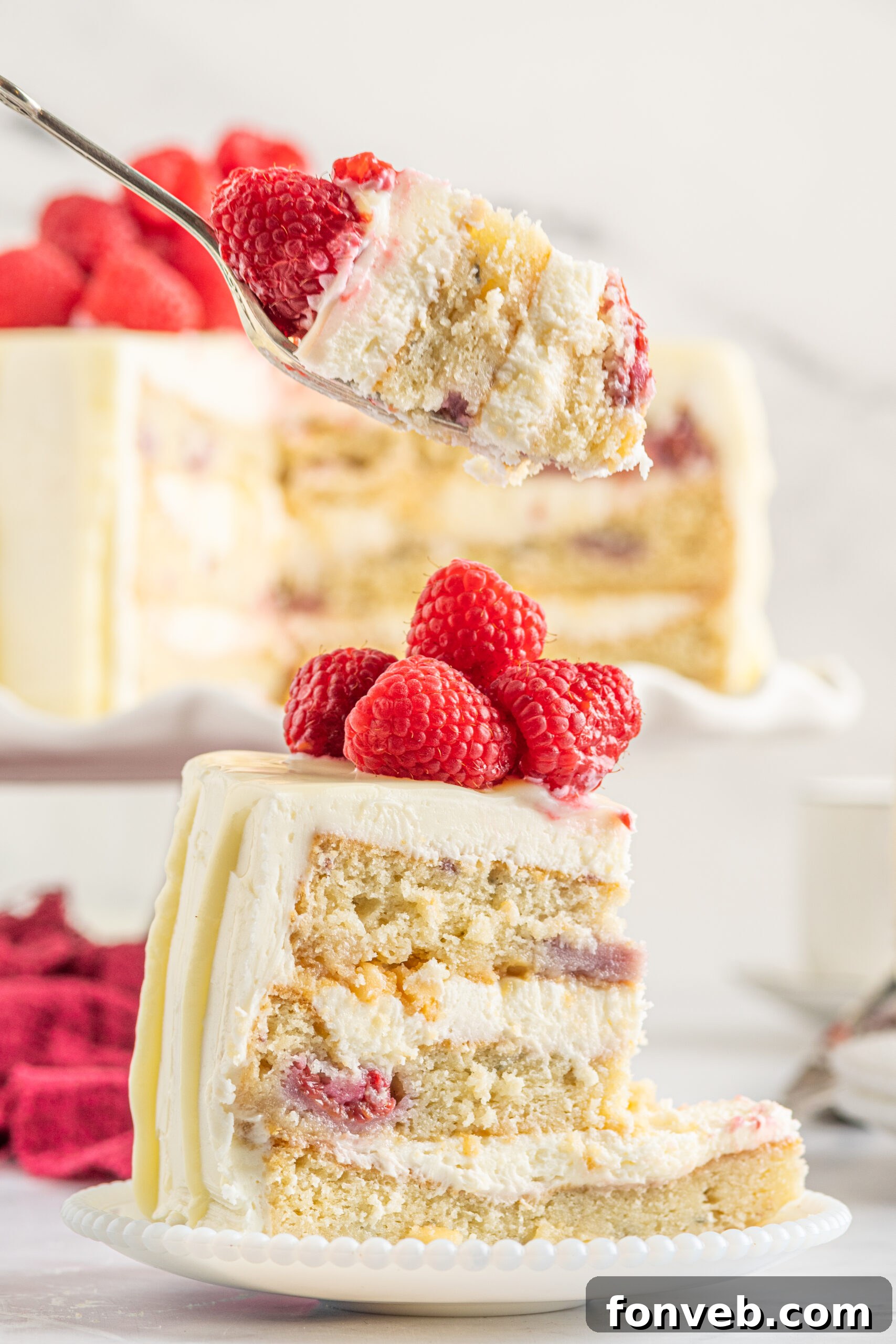 Side view of a bite of White Chocolate Cake with Raspberries on a silver fork.