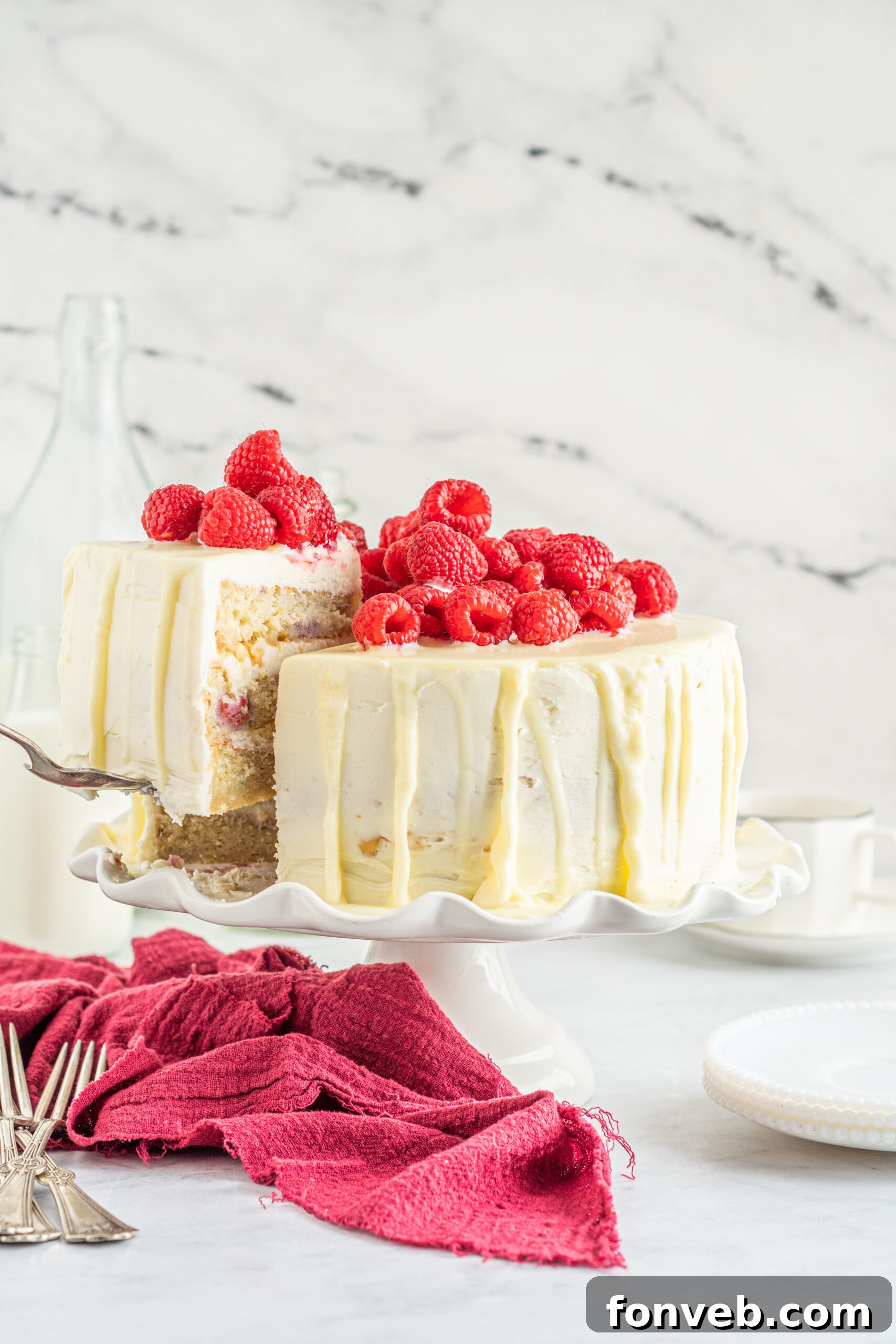 Front view of White Chocolate Cake with Raspberries with a slice being removed by a silver cake server.
