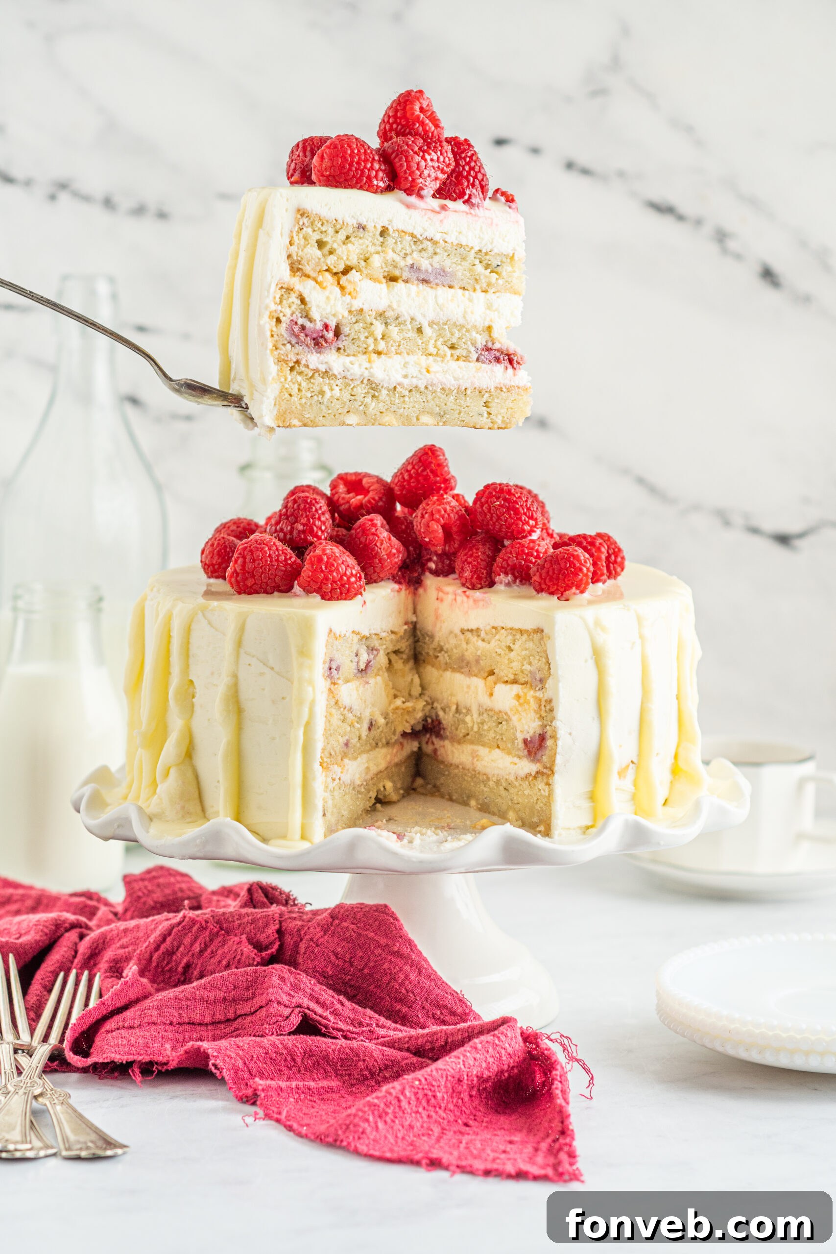 Side view of a slice of White Chocolate Cake with Raspberries on a silver cake server.