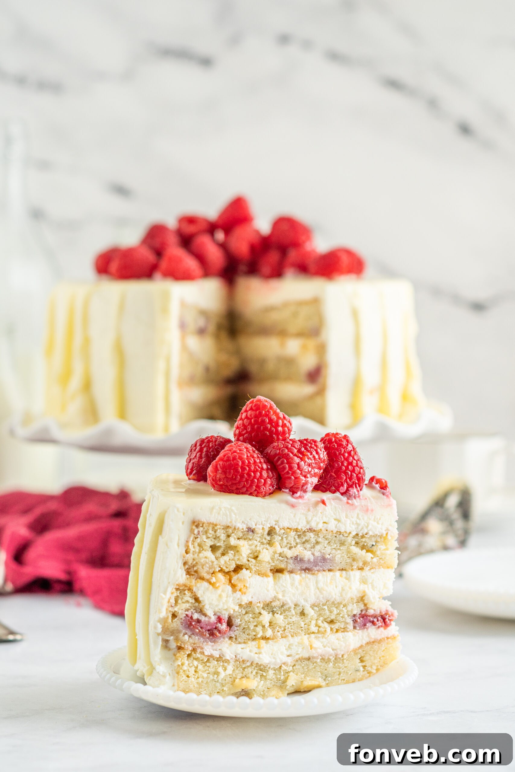 Side view of a slice of White Chocolate Cake with Raspberries on a white plate.