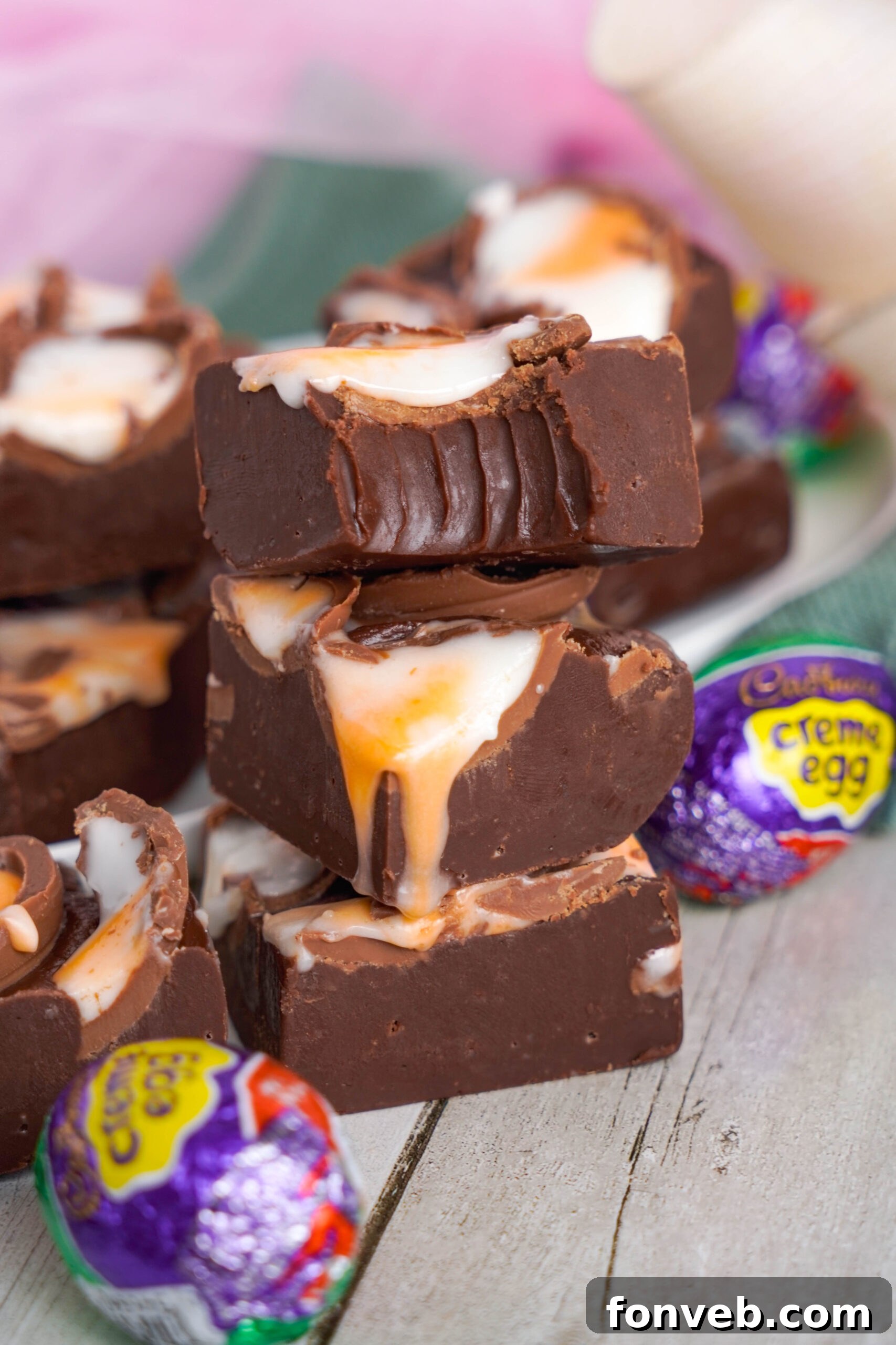 Front view of three pieces of Cadbury Cream Fudge stacked with a bite removed from the top piece.