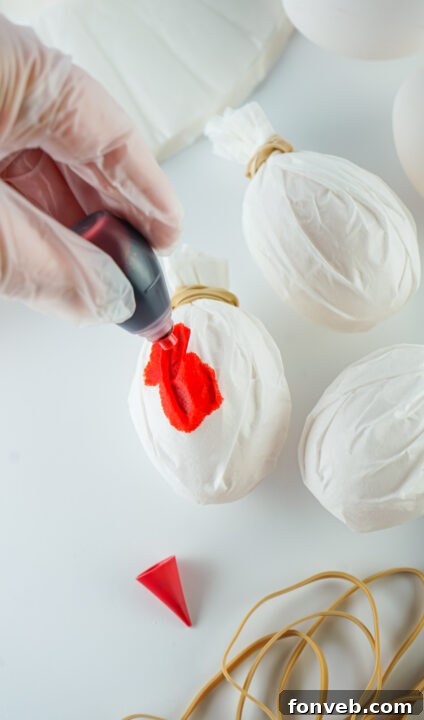 Applying more drops of food coloring to a coffee filter wrapped egg.
