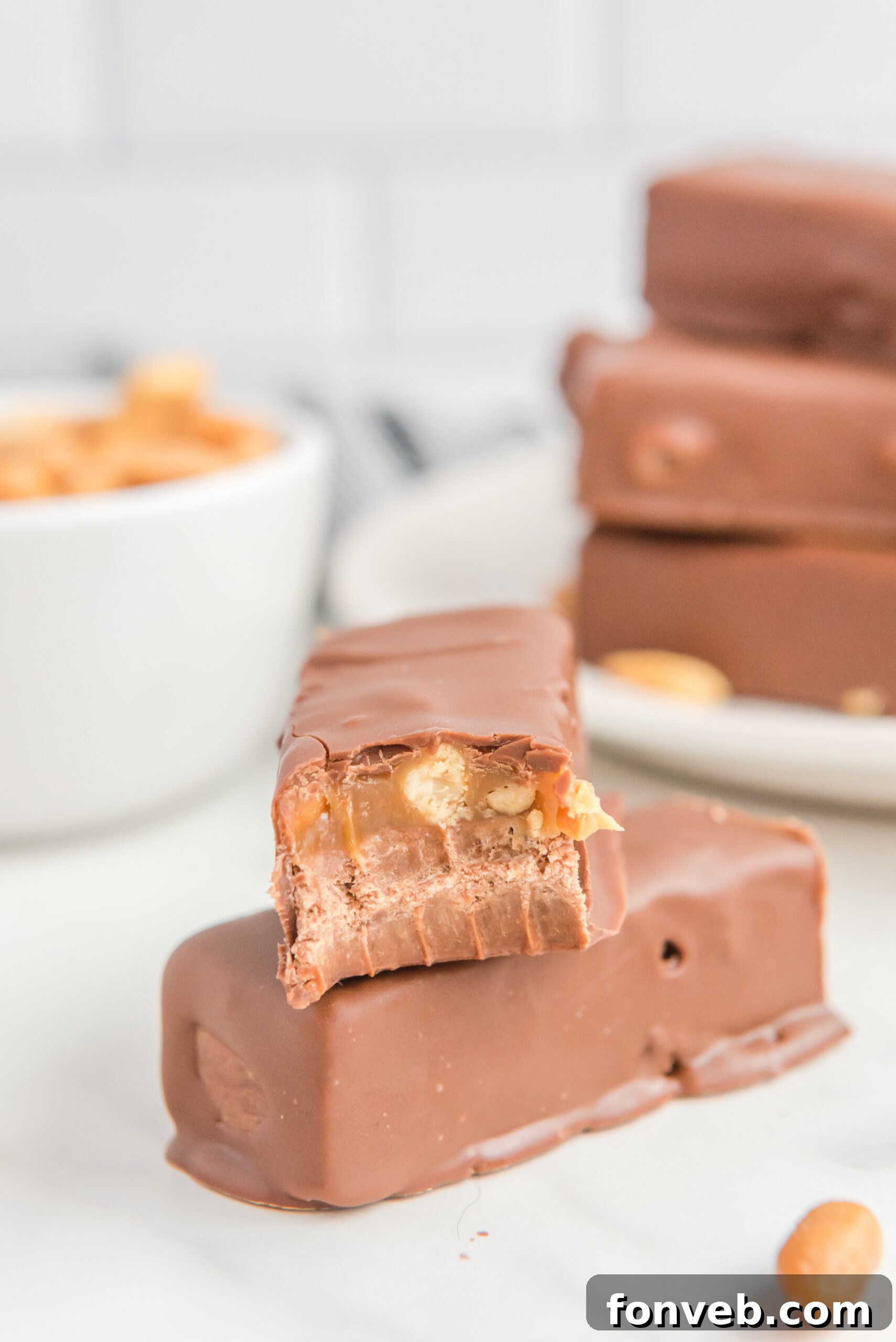A couple of Homemade Snickers Candy Bars artfully placed on a table, one with a delightful bite missing.