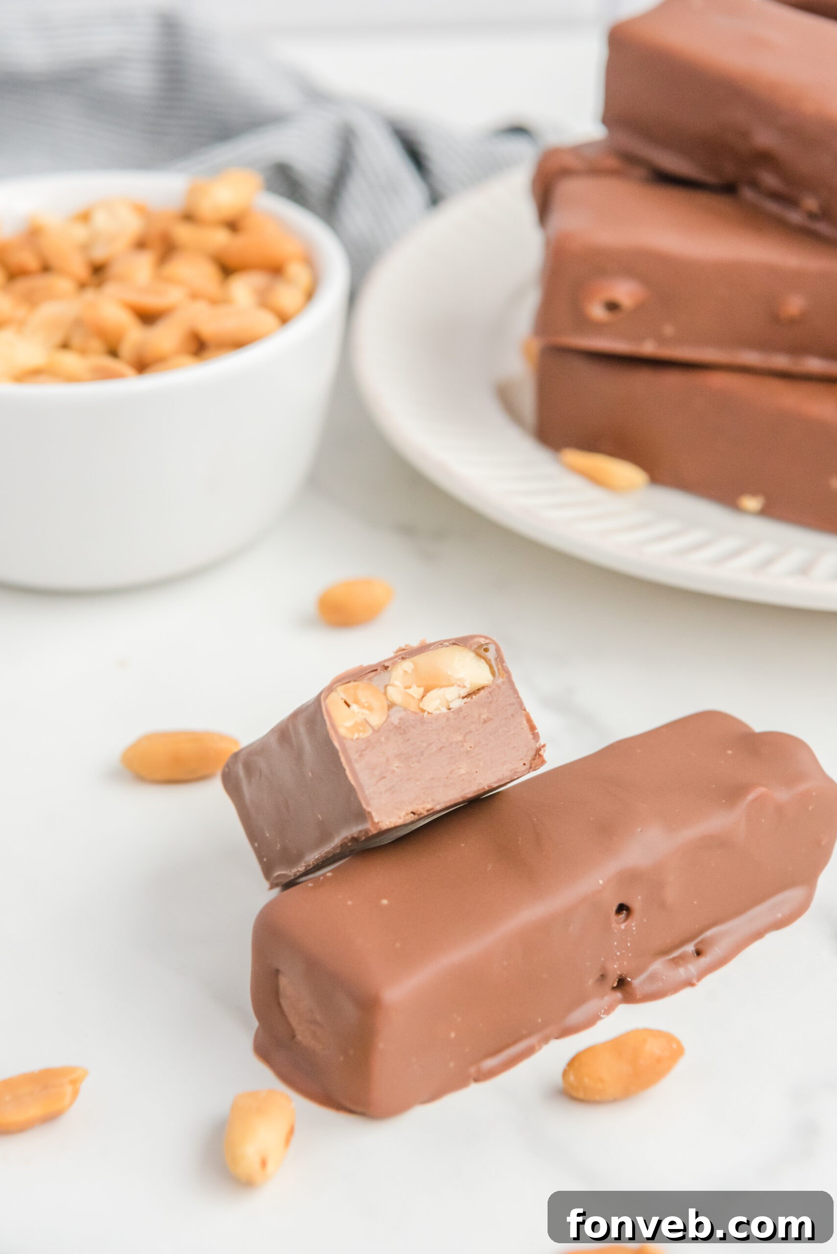 Front view of half of a Homemade Snickers Bar elegantly stacked onto a whole bar, revealing its inviting layers.