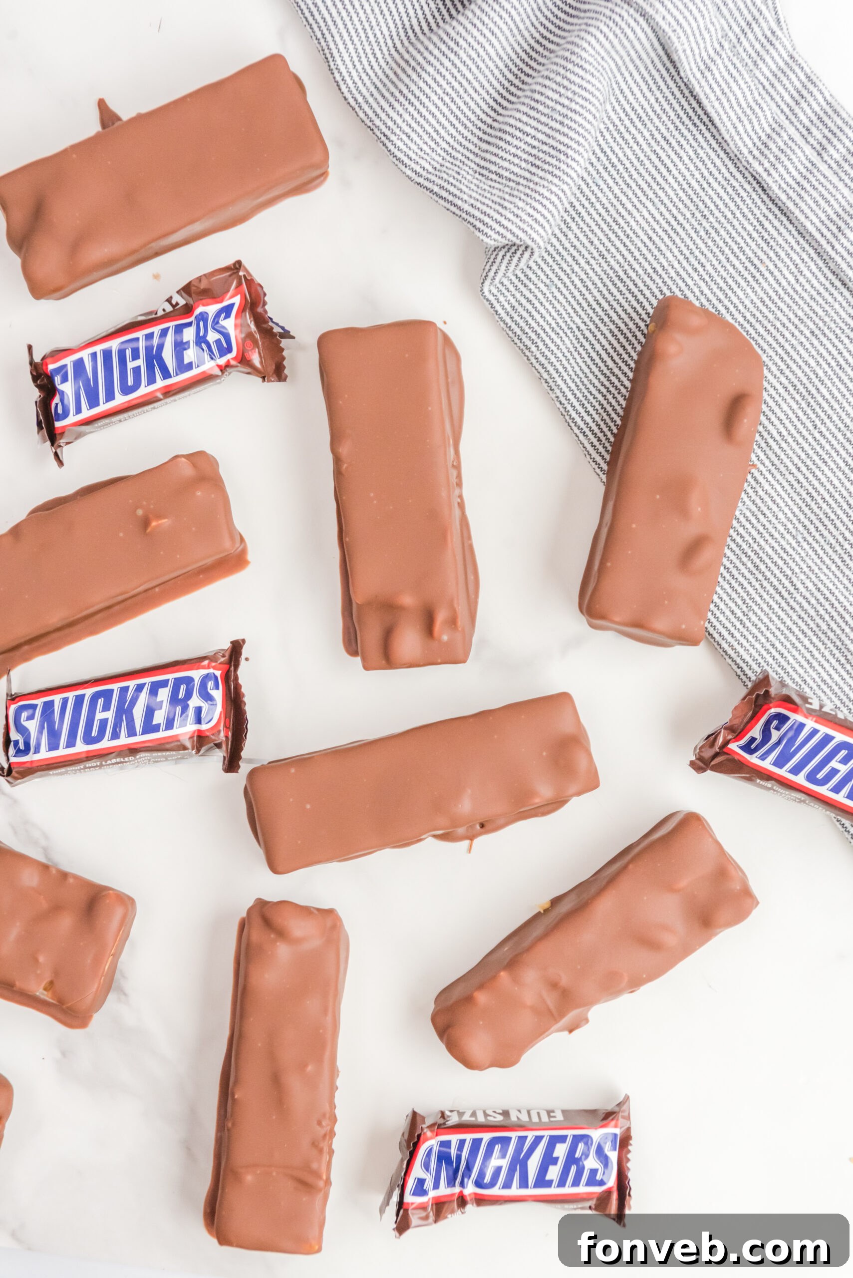 Overhead view of several perfectly formed Homemade Snickers Bars, highlighting their uniform size and glistening chocolate coating.