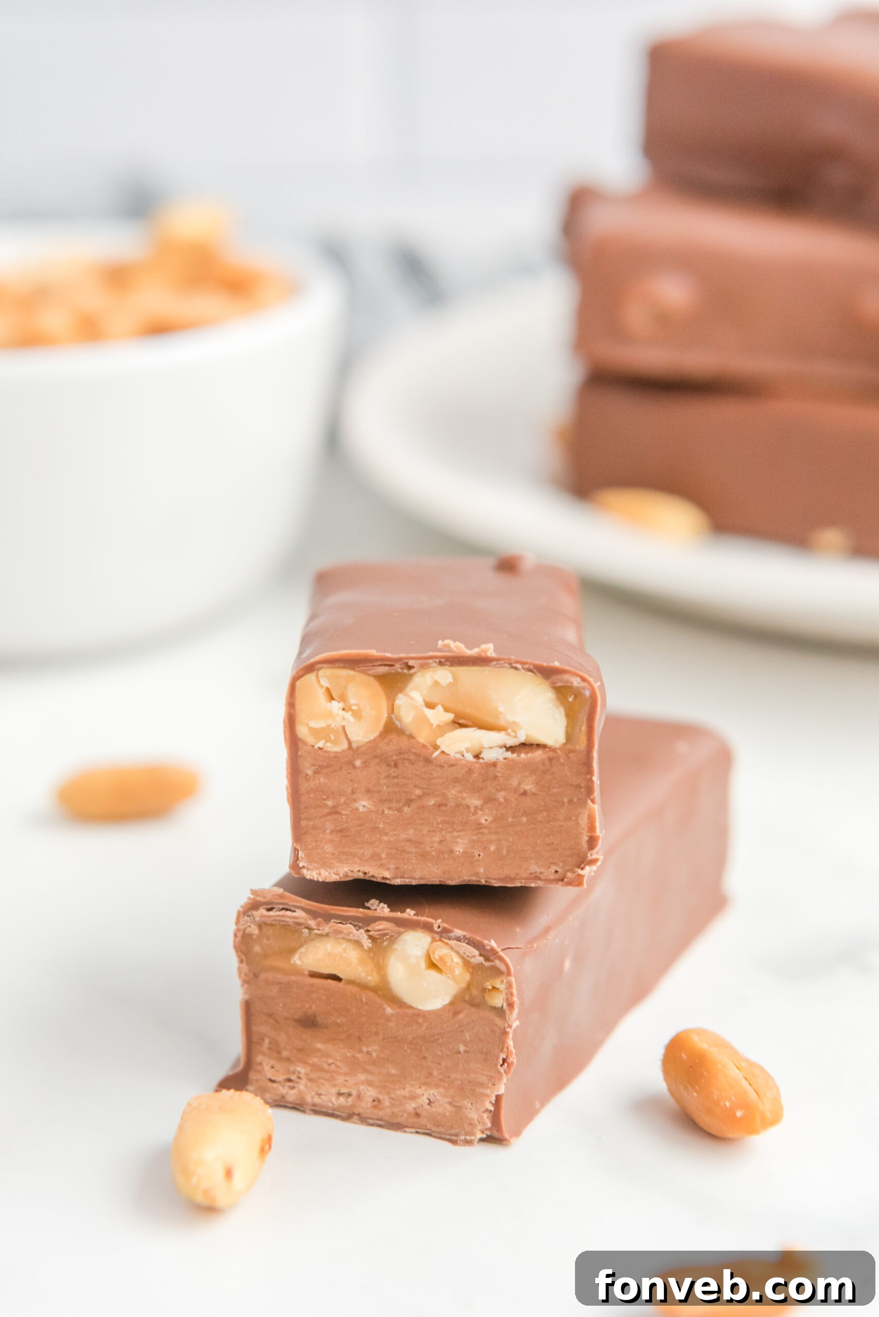 Front view of two halves of Homemade Snickers Bars expertly stacked, emphasizing the distinct layers.