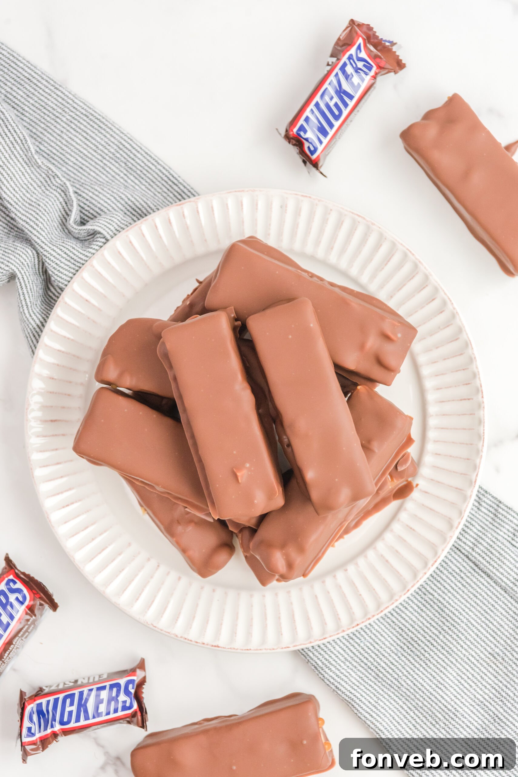 Overhead view of Homemade Snickers Bars neatly stacked on a white plate, ready to be served or enjoyed as a personal indulgence.