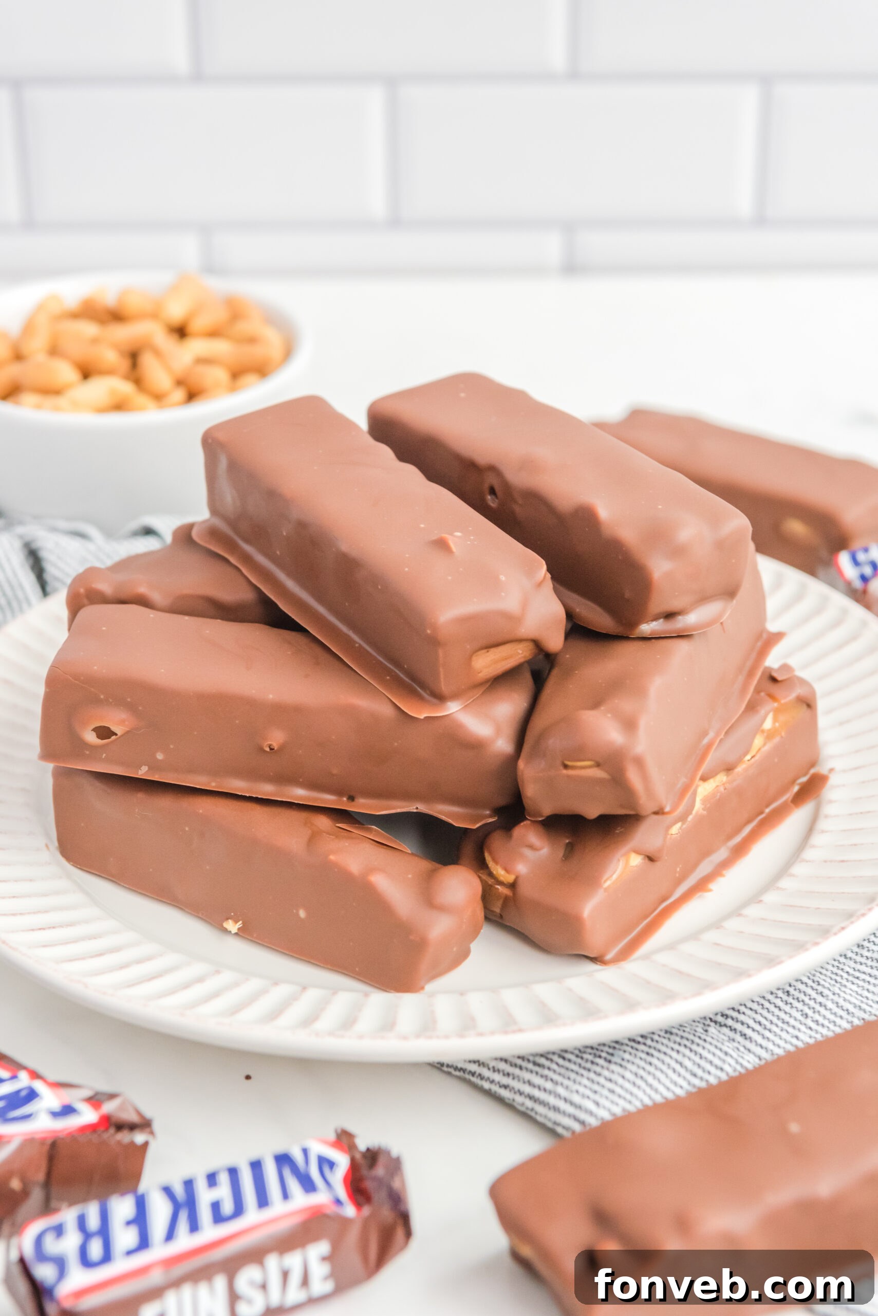 Front view of several Homemade Snickers Bars stacked artistically on a white plate, highlighting their appetizing cross-section.