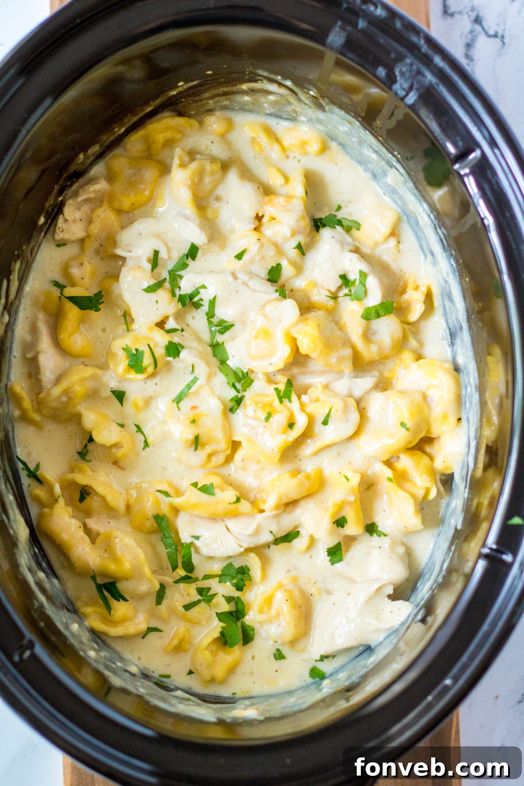 Overhead view of Slow Cooker Chicken Tortellini in a crock pot, garnished with fresh herbs.