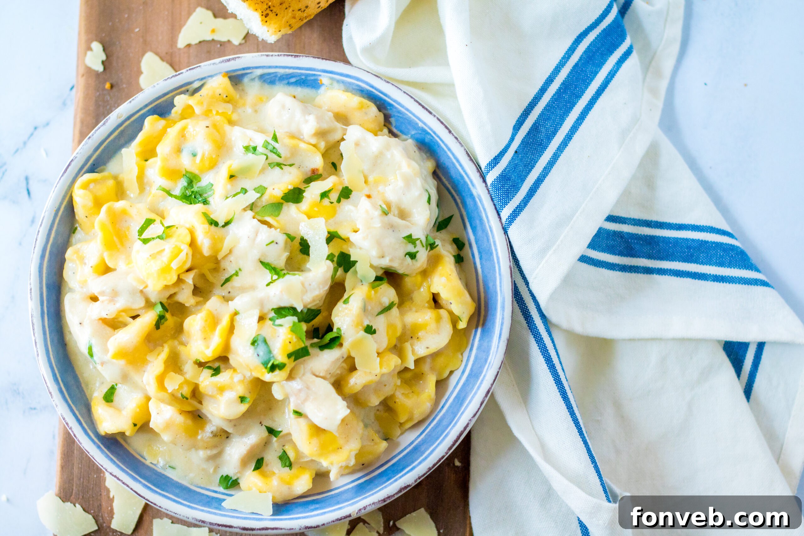 Overhead view of Slow Cooker Chicken Tortellini in a white and blue bowl with garlic bread and salad.