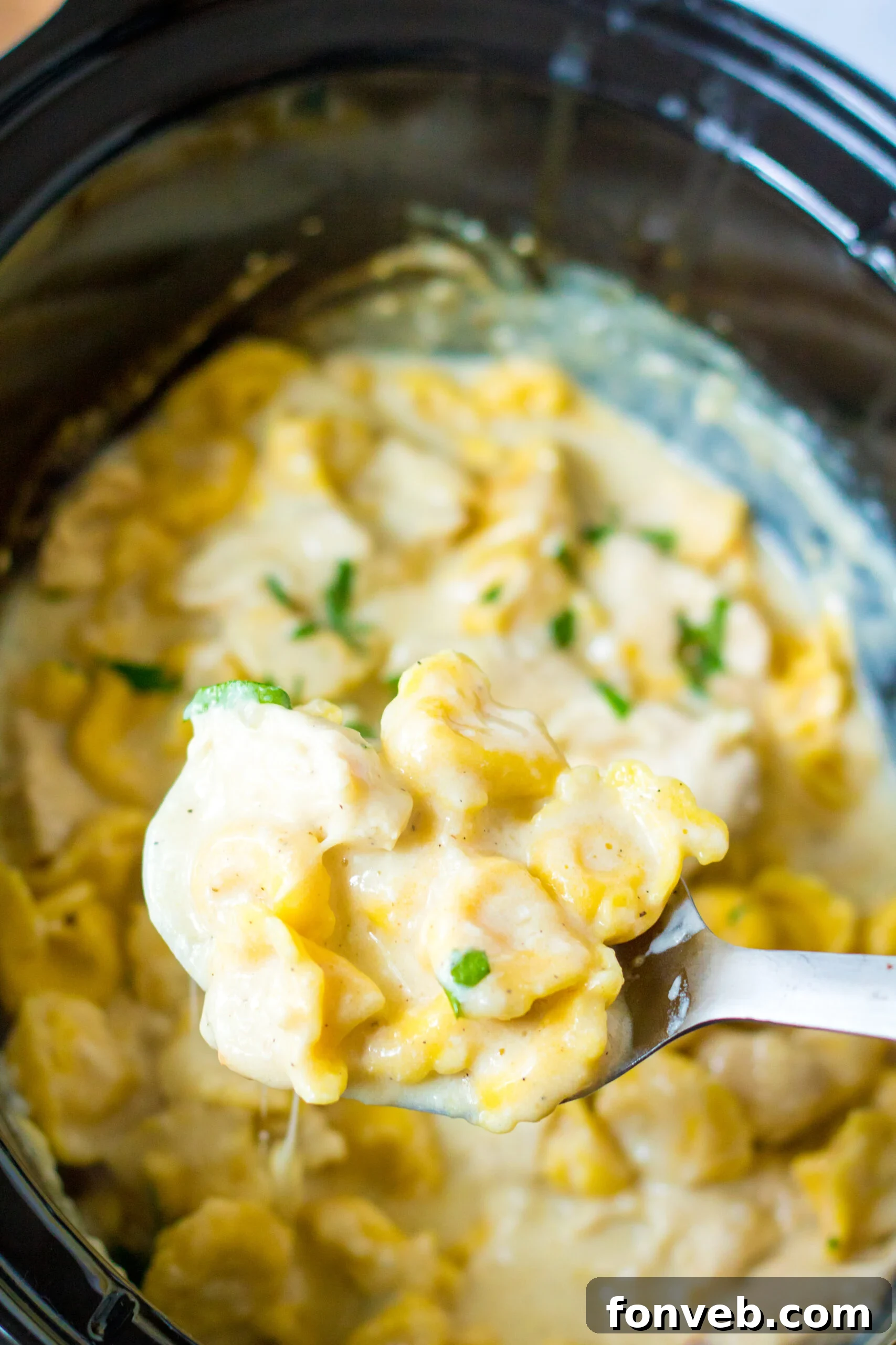 Overhead view of a bite of Slow Cooker Chicken Tortellini on a silver spoon, ready to be eaten.