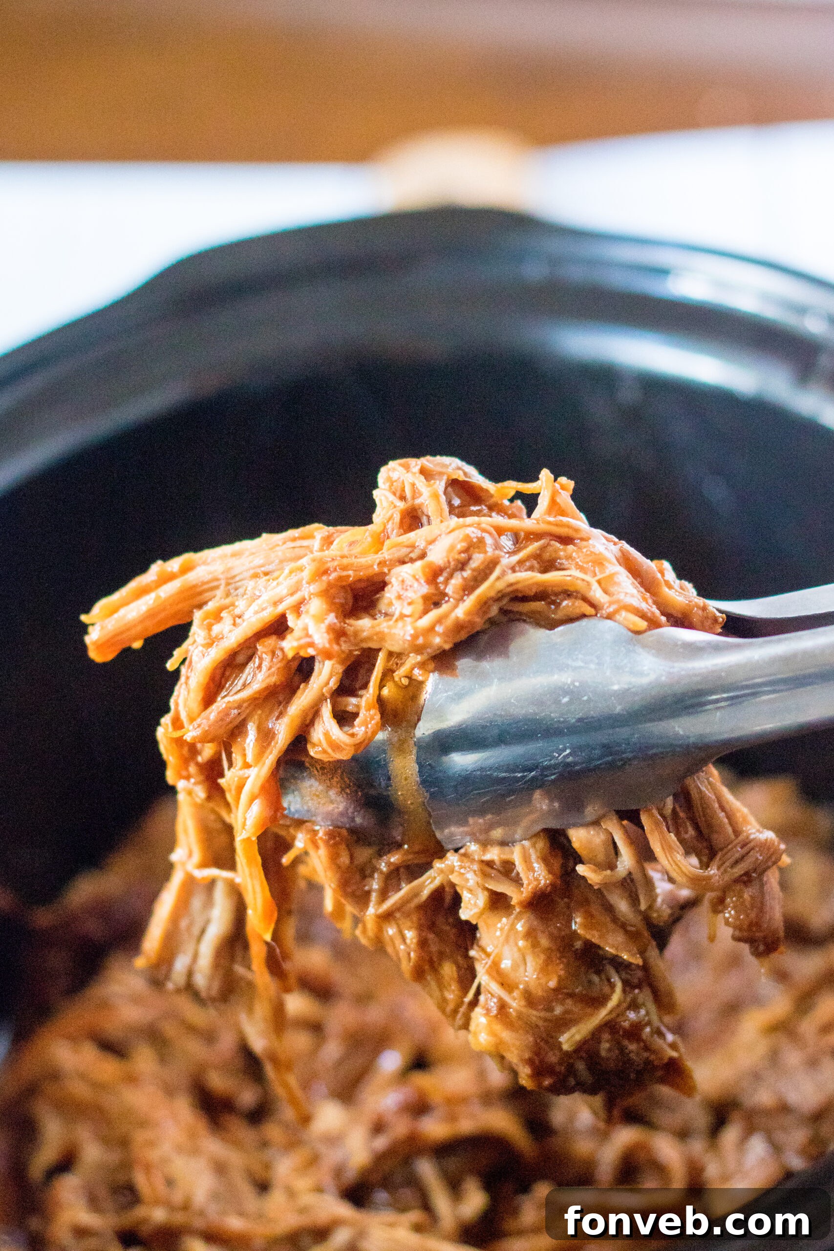 Sticky Sweet Slow Cooker Coke Pulled Pork 5 Front view of silver tongs holding a serving of Slow Cooker Cola Pulled Pork.