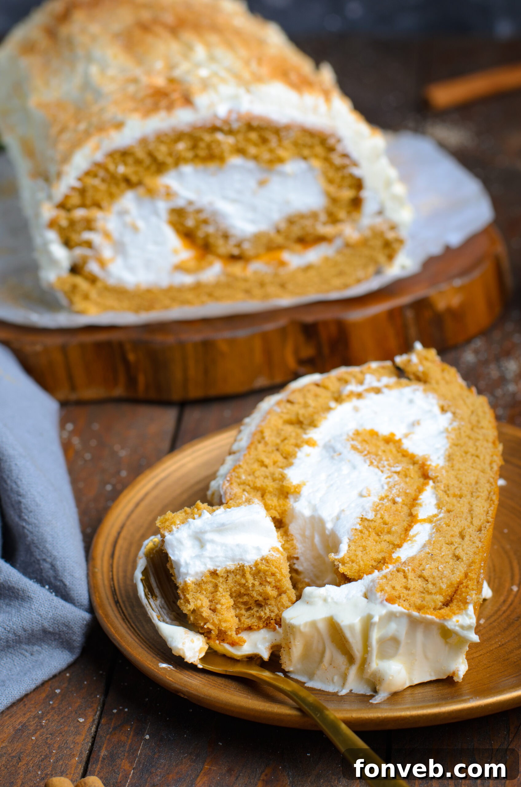 Close up view of a slice of Gingerbread Cake Roll on a brown plate with a bite removed by a gold fork.
