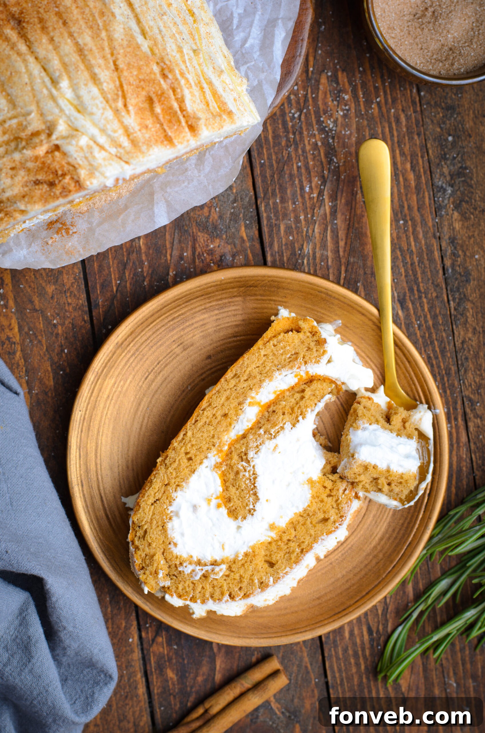 Overhead view of a slice of GIngerbread Cake Roll on a brown plate with a bite removed by a gold spoon.