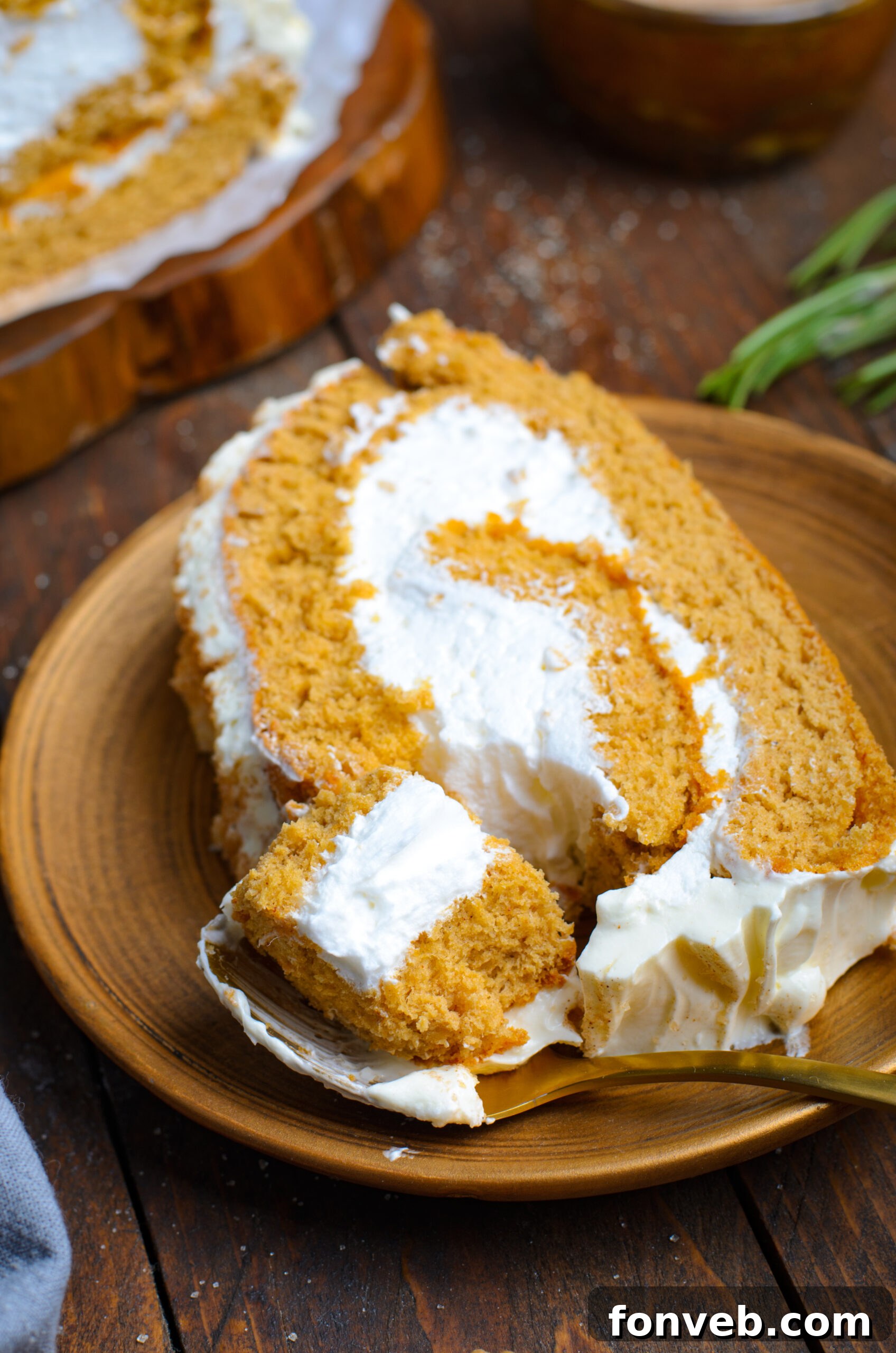 Close up view of a slice of GIngerbread Cake Roll on a brown plate with a bite removed by a gold fork.
