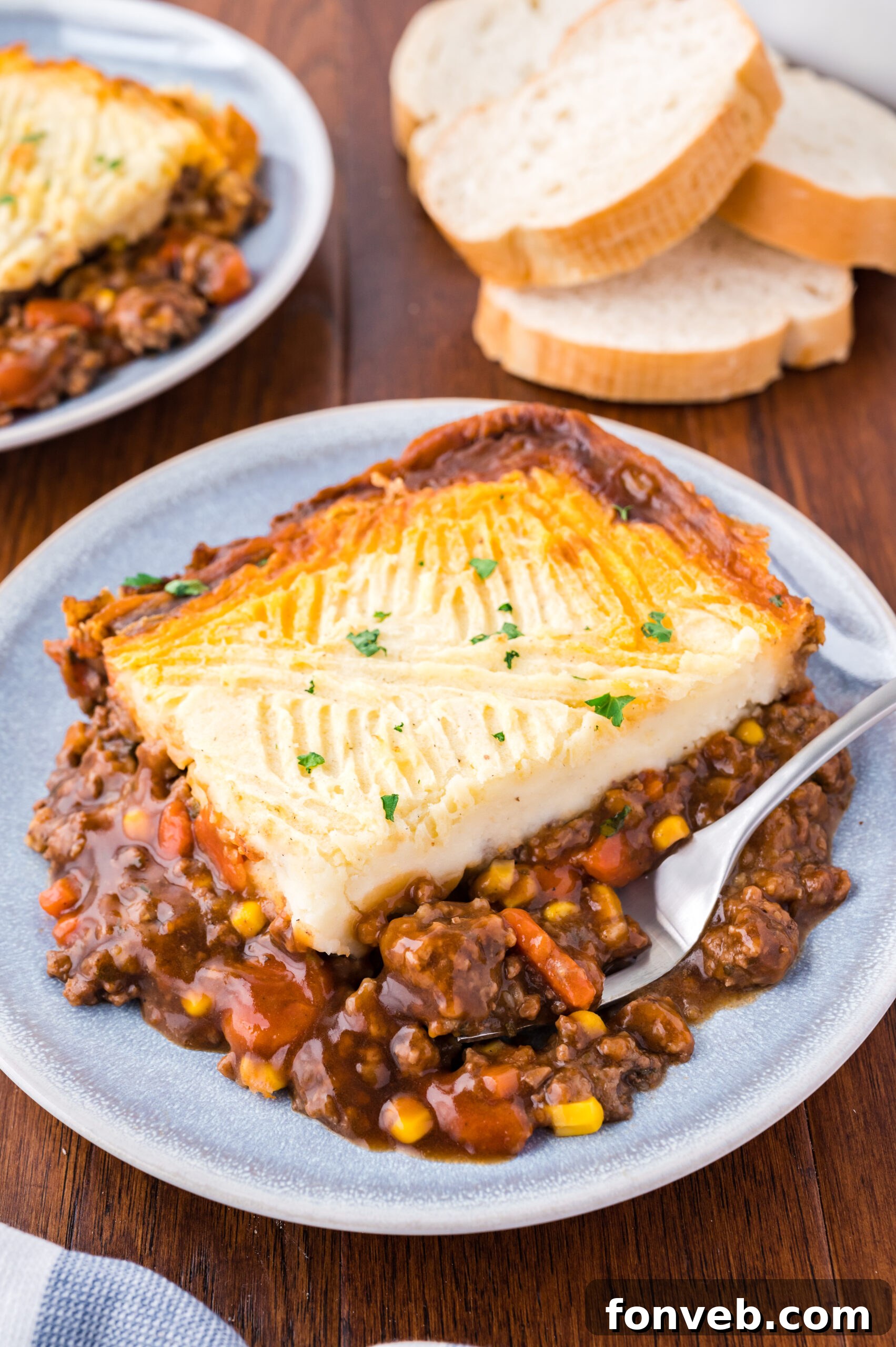 A serving of Shepherd's Pie on a gray and white plate with a silver spoon, highlighting the mashed potato topping and rich filling.