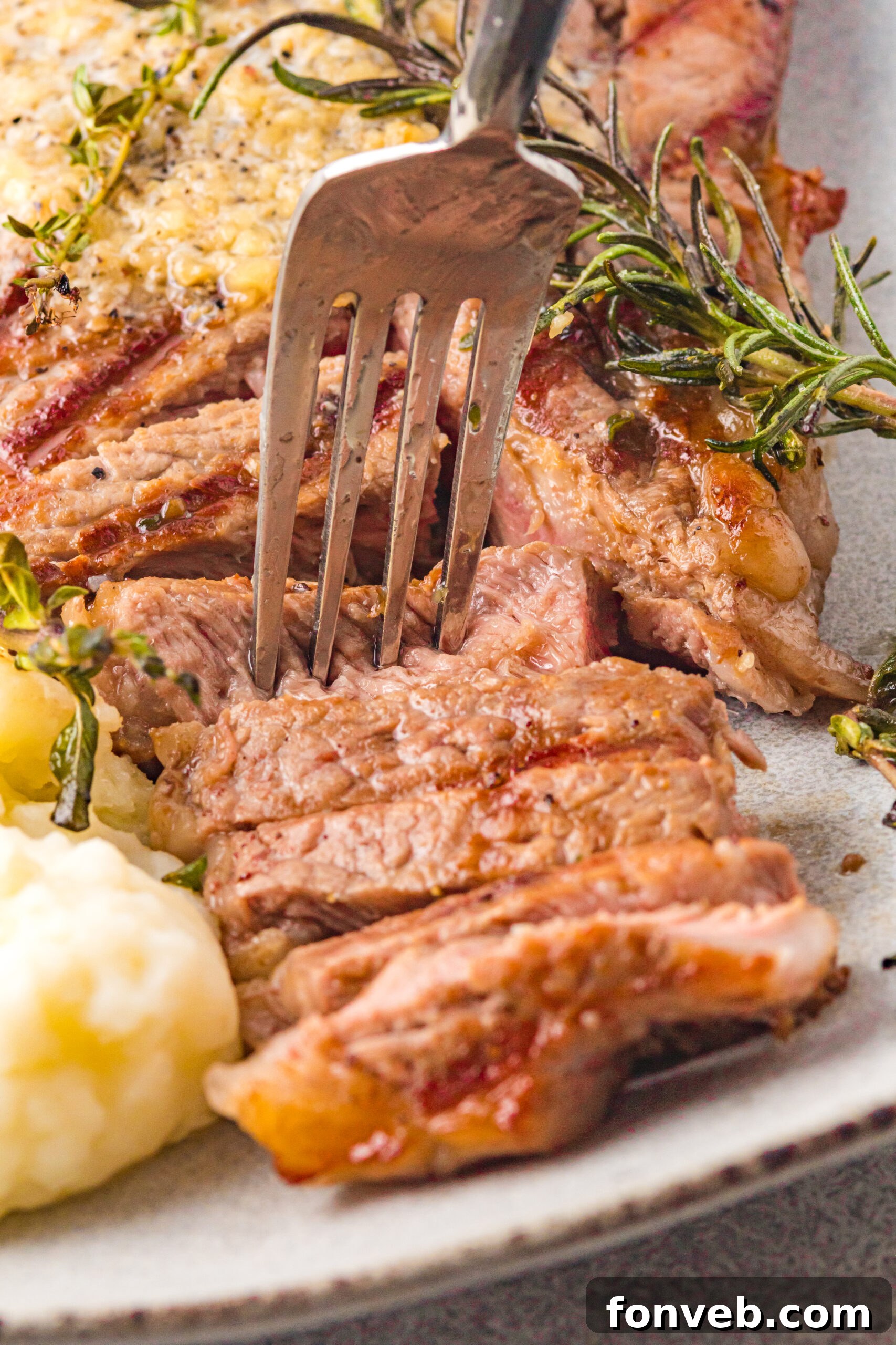 Close up view of a silver fork removing a bite of T Bone Steak.