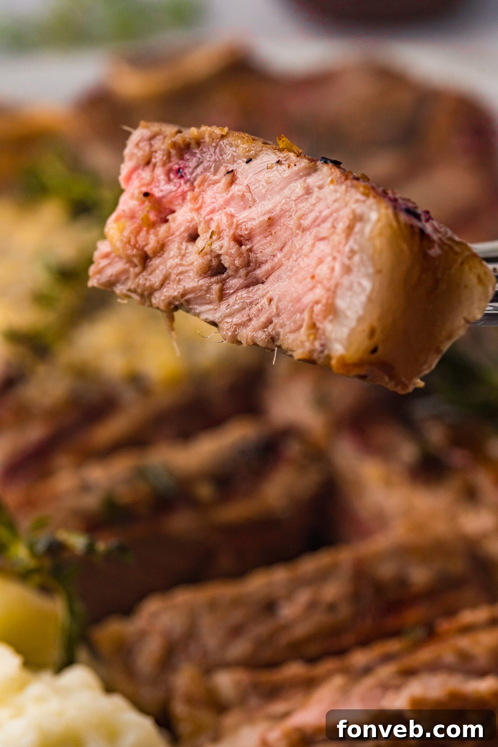 Close up view of a bite of T Bone Steak on a silver fork.