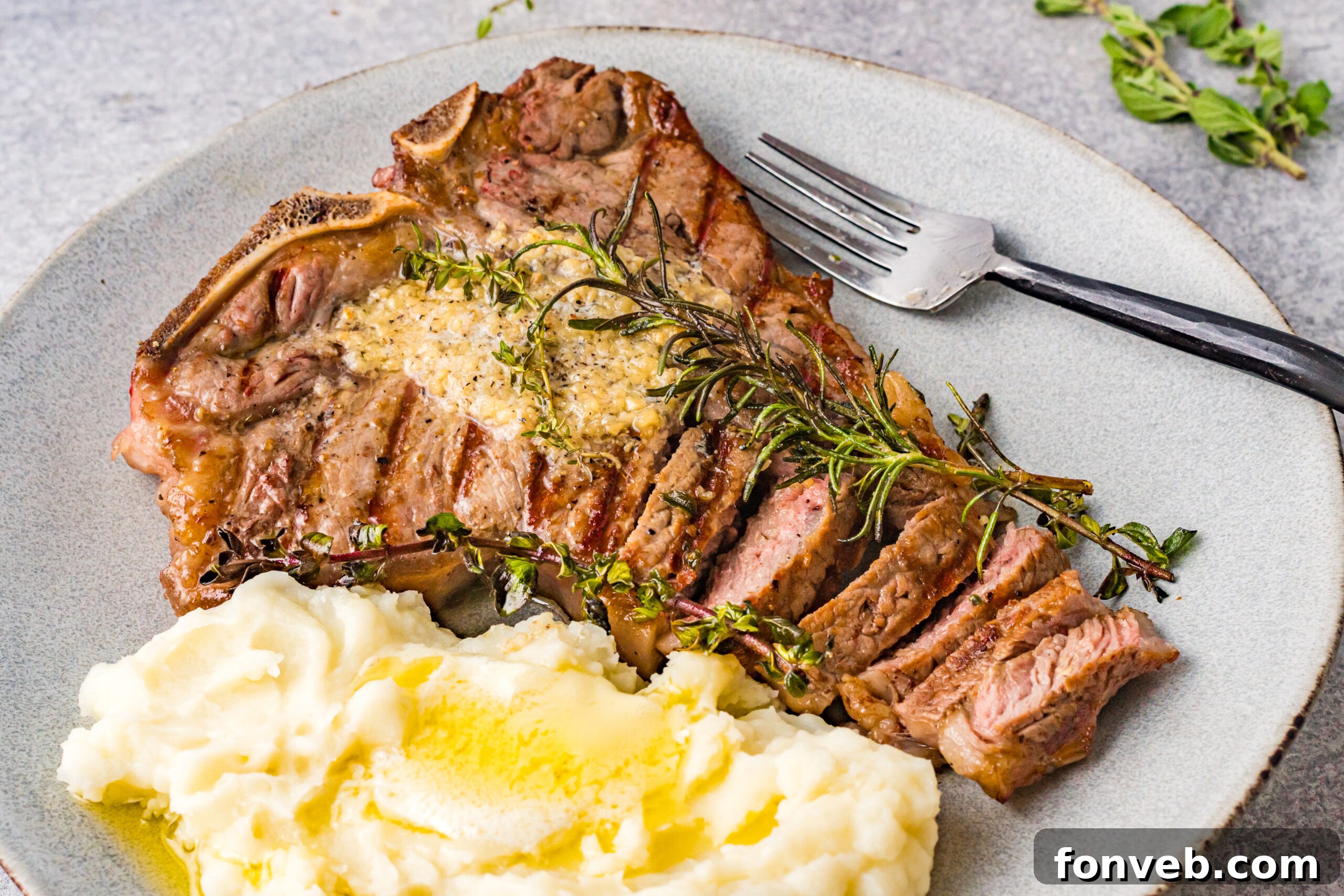 Overhead view of T Bone Steak on a white plate served with mashed potatoes.