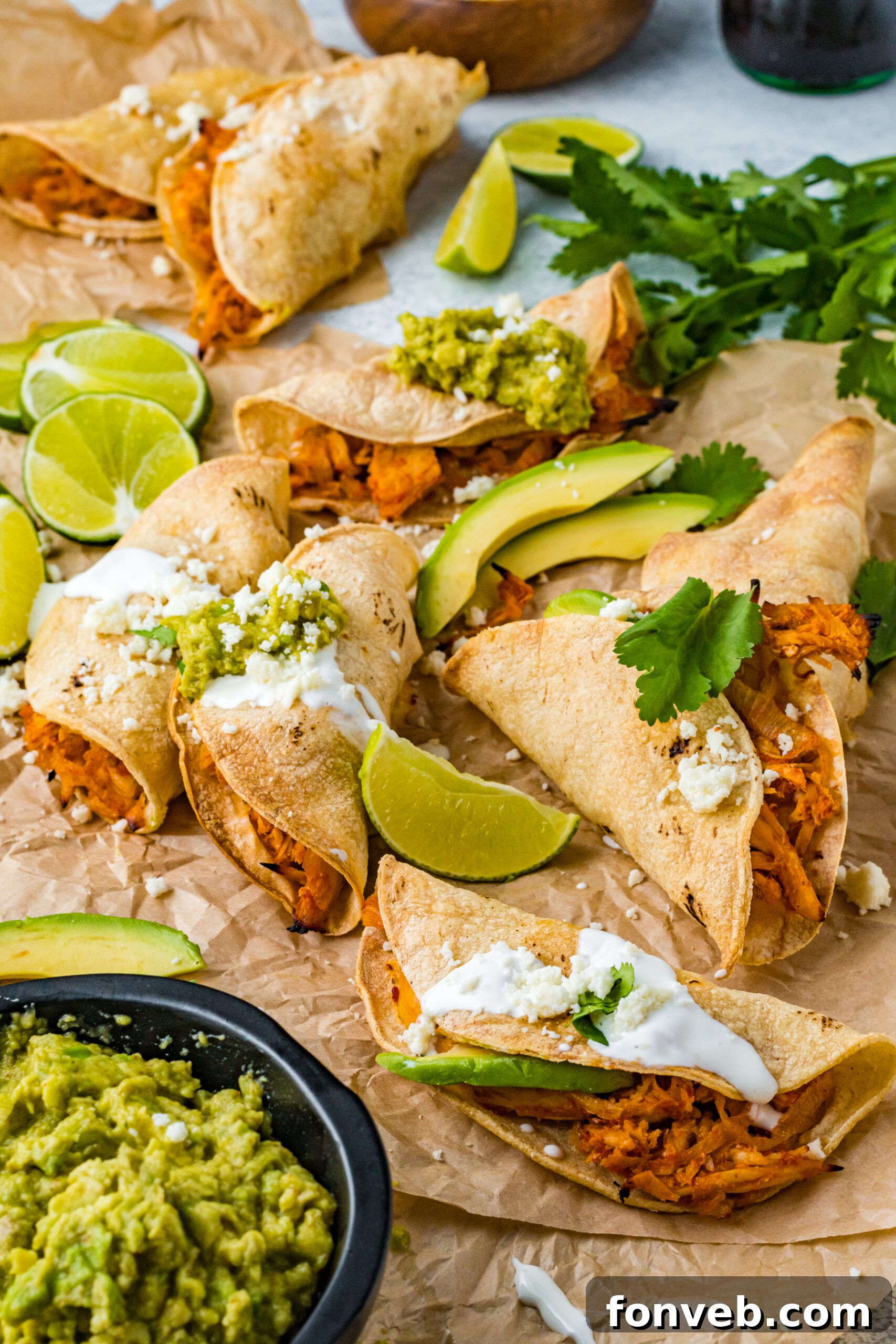 Front view of Crispy Tinga Tacos on a piece of parchment paper surrounded by lime and avocado slices.