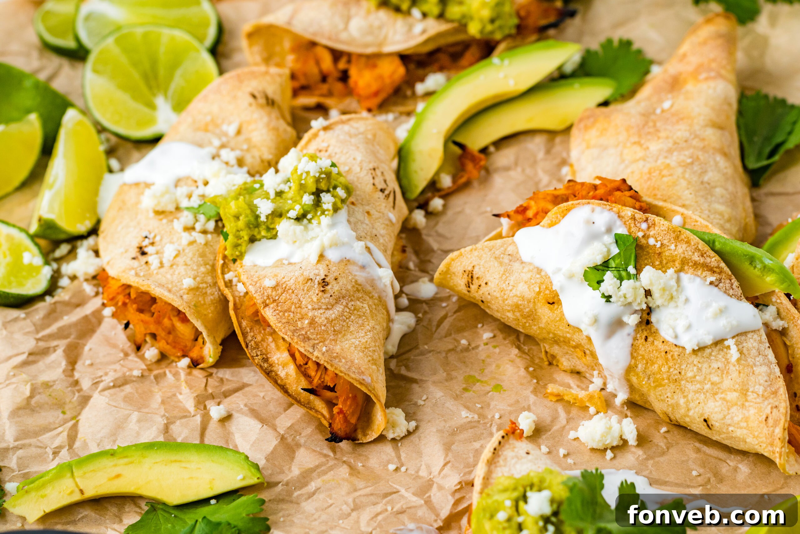 Front view of Crispy Tinga Tacos on a piece of parchment paper surrounded by lime and avocado slices.