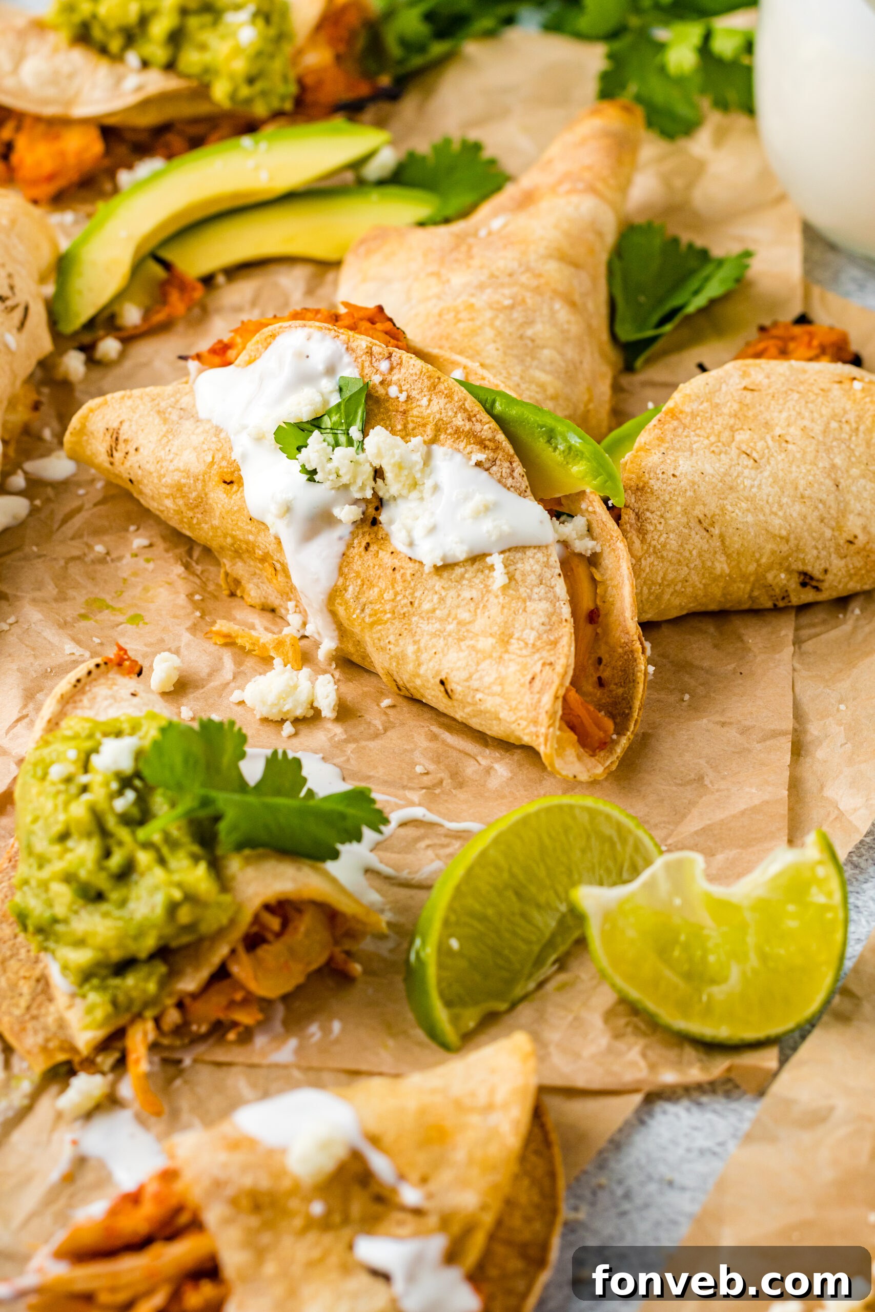 Front view of Crispy Tinga Tacos on a piece of parchment paper surrounded by lime and avocado slices.