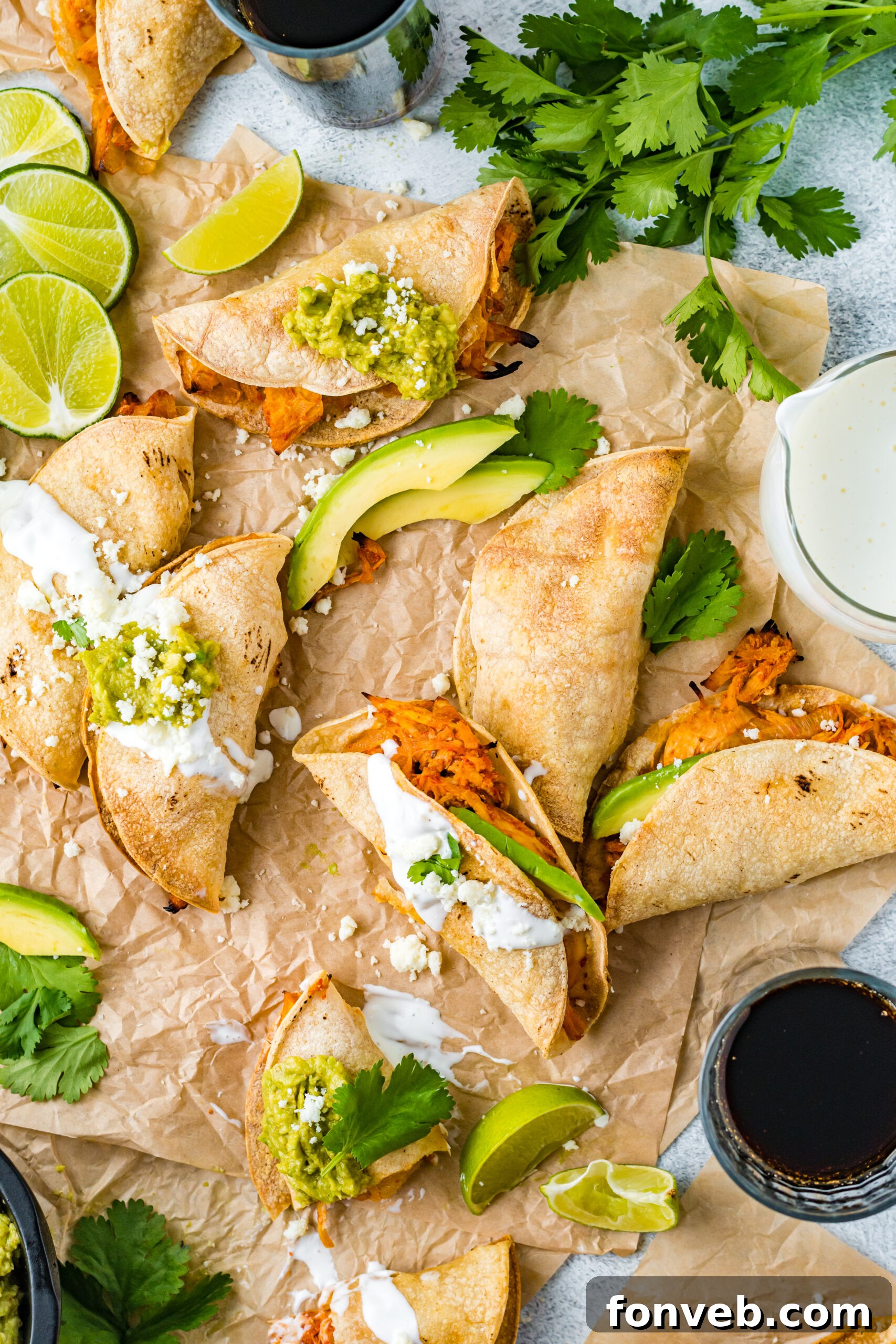 Overhead view of Crispy Tinga Tacos on a piece of parchment paper surrounded by lime and avocado slices.